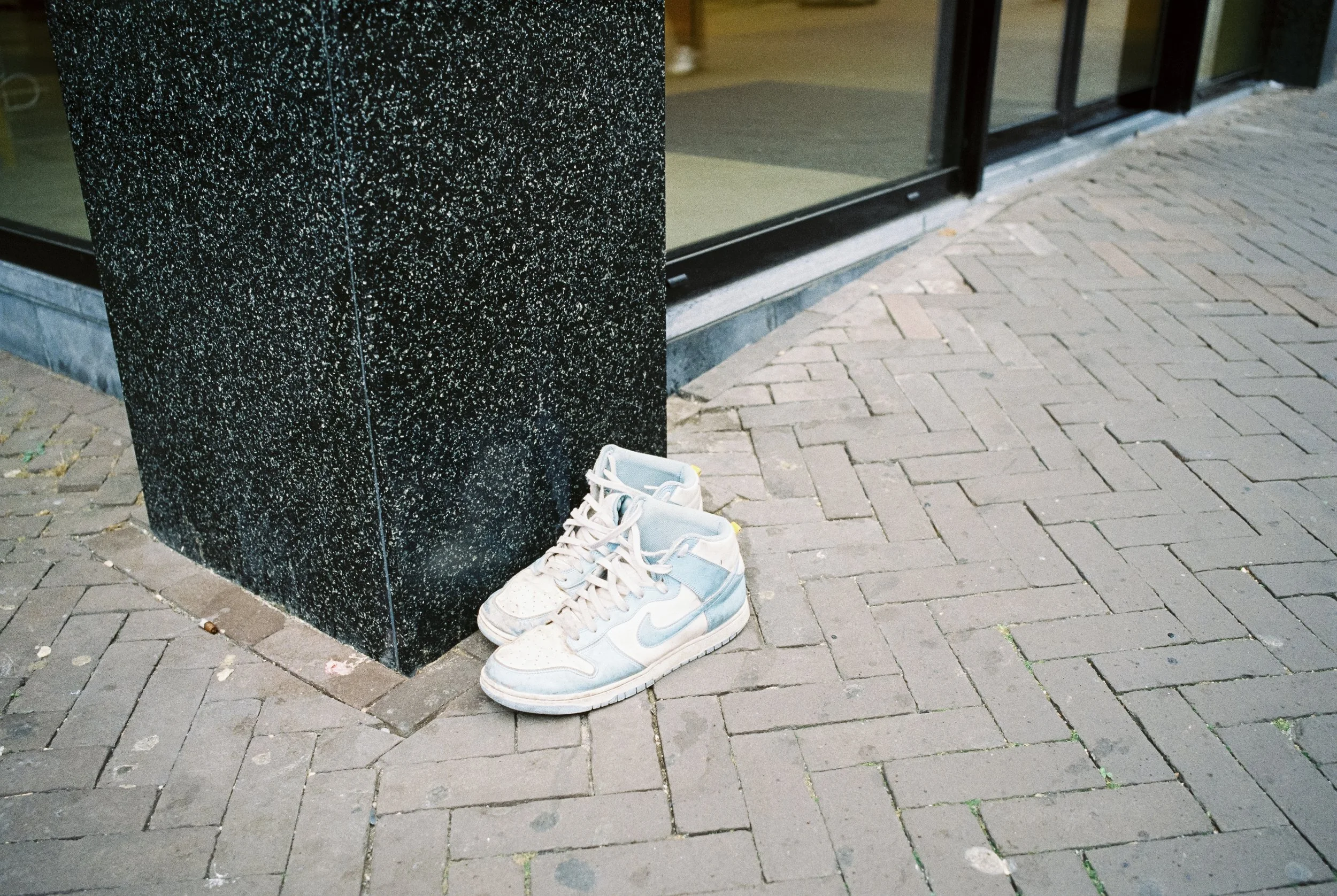 Ein Paar veraltete weiße und blaue Turnschuhe steht außerhalb eines Geschäfts auf gepflastertem Bürgersteig.