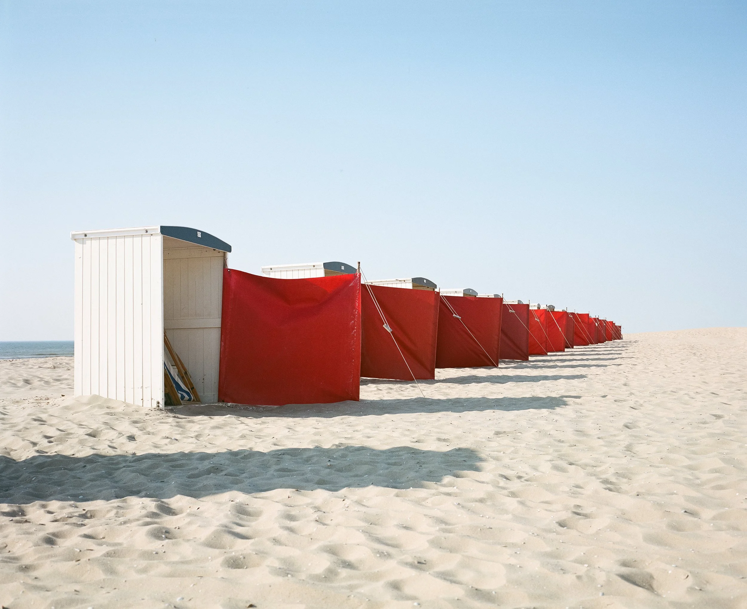 Strand mit mehreren roten Strandkörben, die aneinandergereiht sind, unter einem blauen Himmel.
