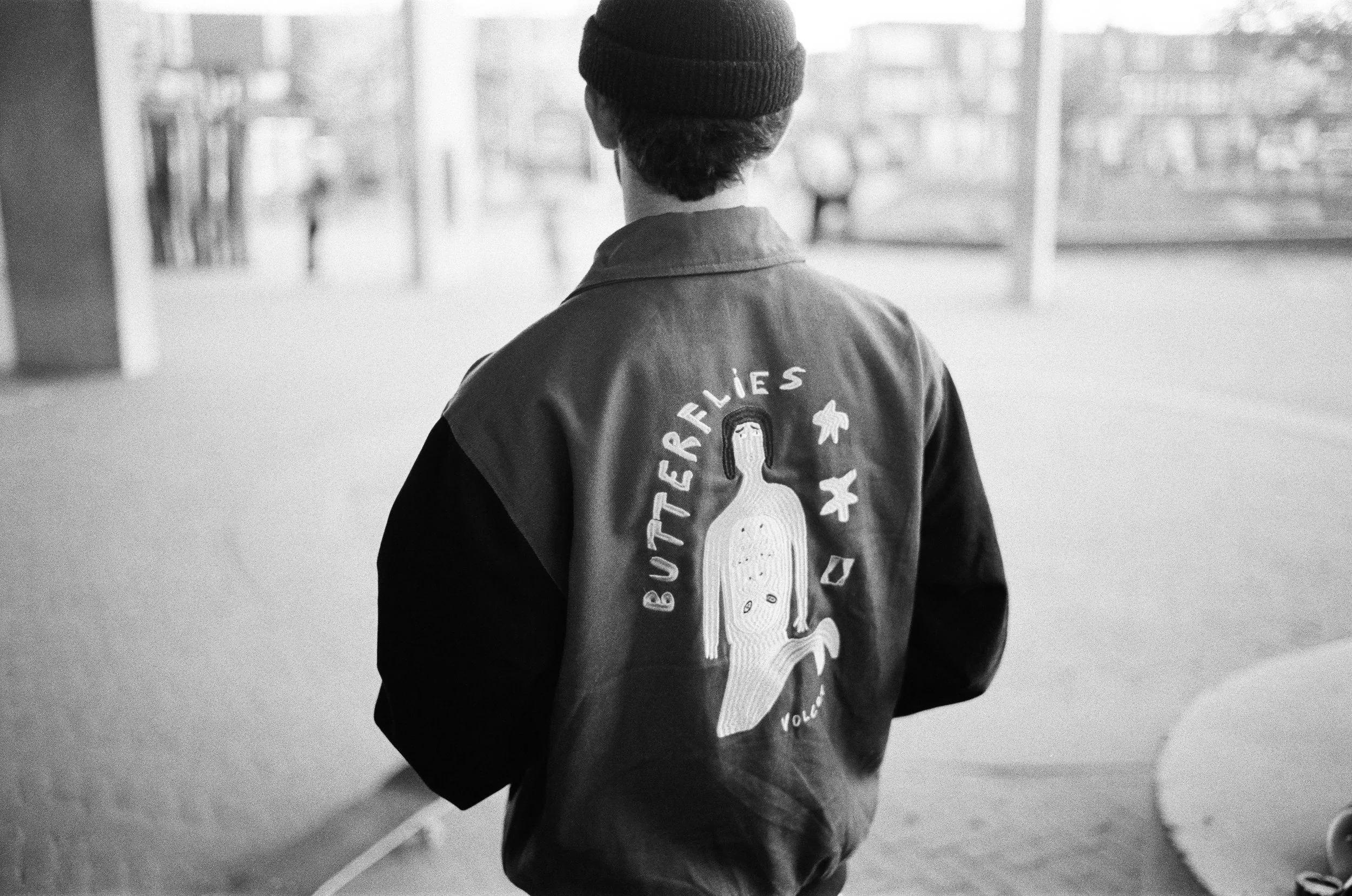 Ein Mann trägt eine Jacke mit einem aufgenähten Design und der Aufschrift "BUTTERFLIES" auf dem Rücken, während er nach draußen schaut.