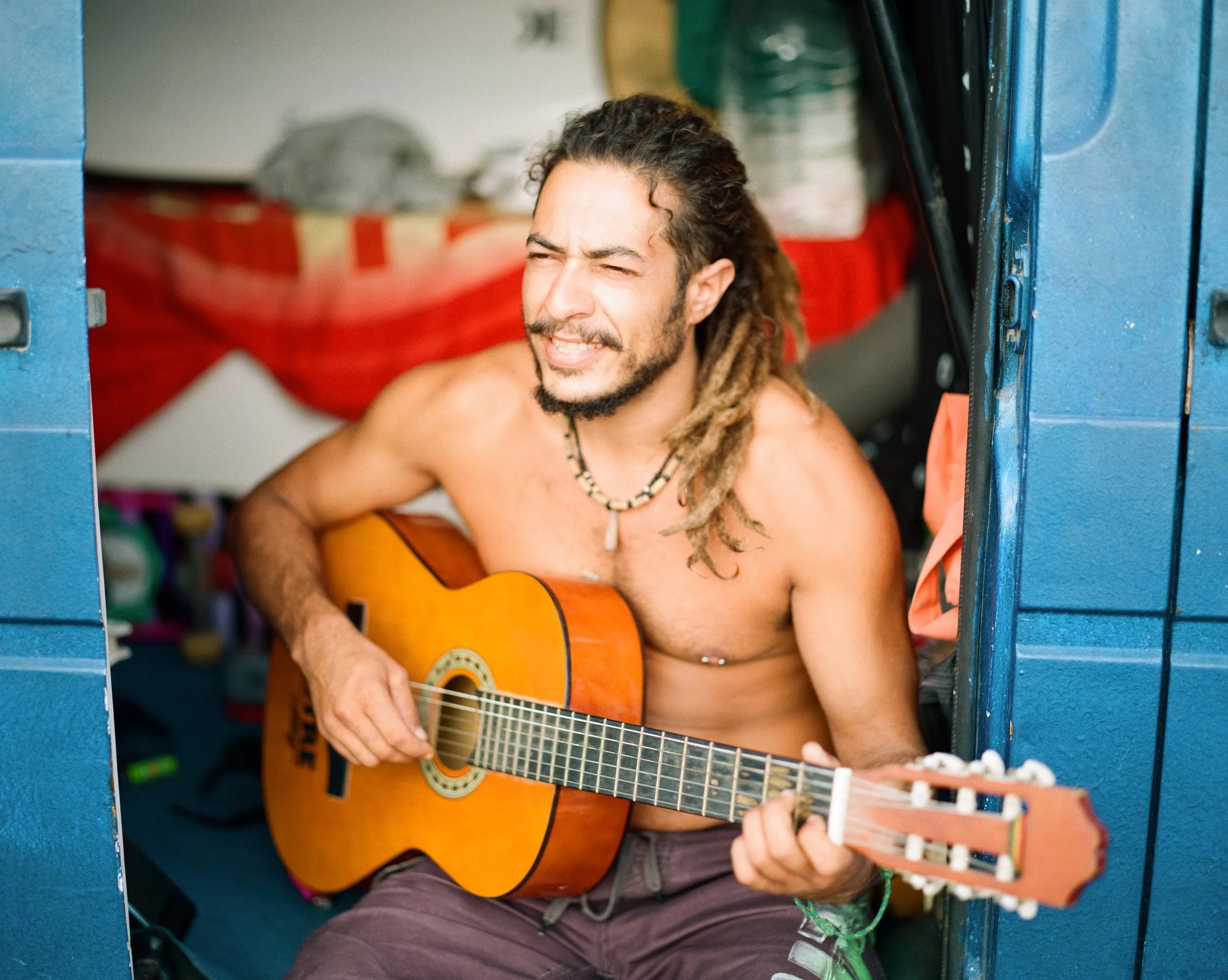 Ein Mann mit Dreadlocks sitzt in einem offenen Schrank und spielt Gitarre.
