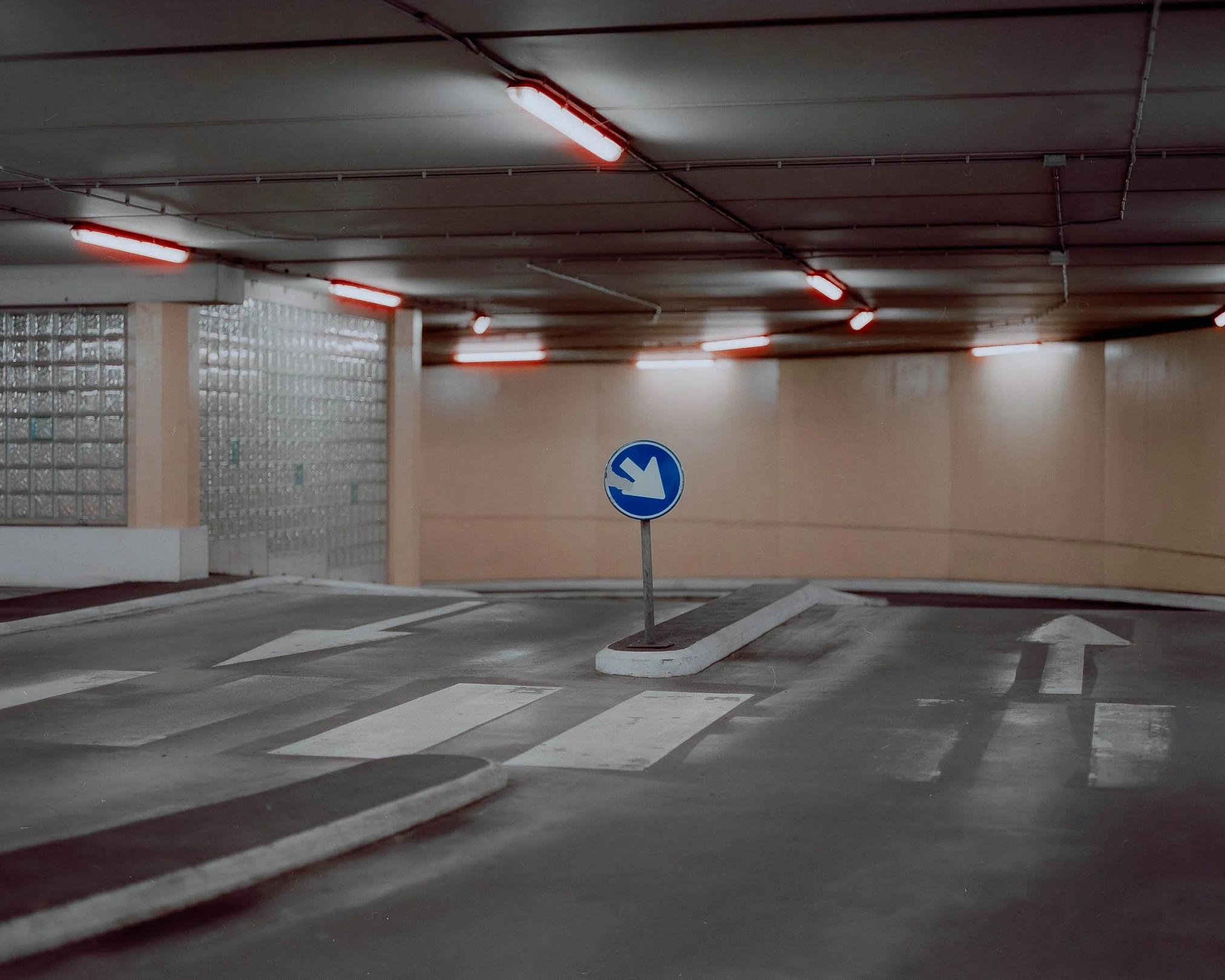 Ein leeres, unterirdisches Parkhaus mit weißen Straßenmarkierungen, Verkehrsschildern und roten Leuchten an der Decke.