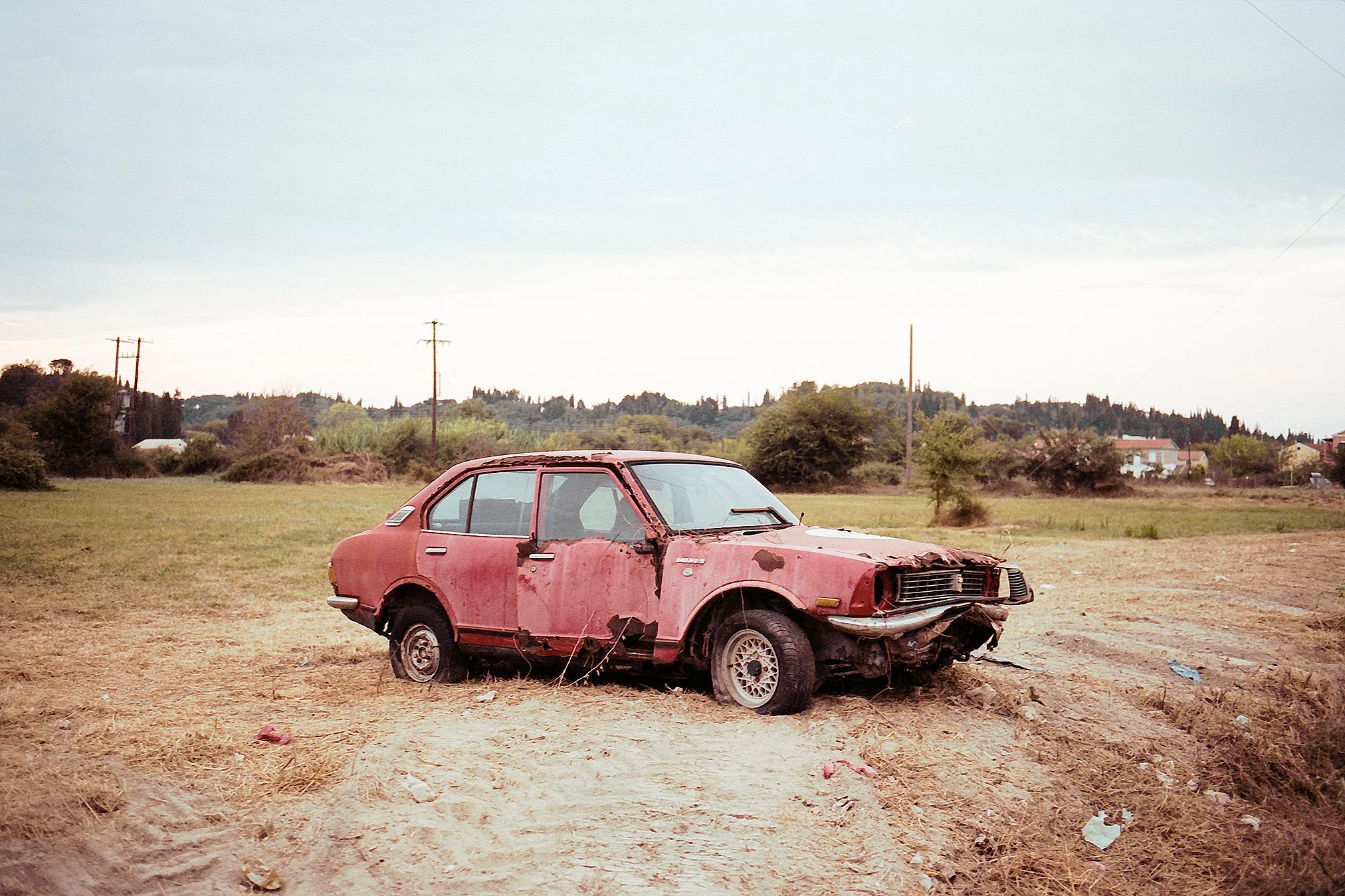 Ein verfallener, roter, sowjetischer Automobil in einem verlassenen Feld, beschädigt und verrottend.