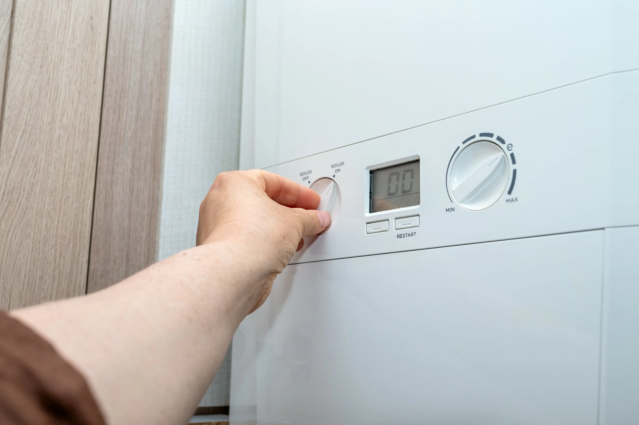 A person turning on a white boiler with a digital display, control knob, and buttons.