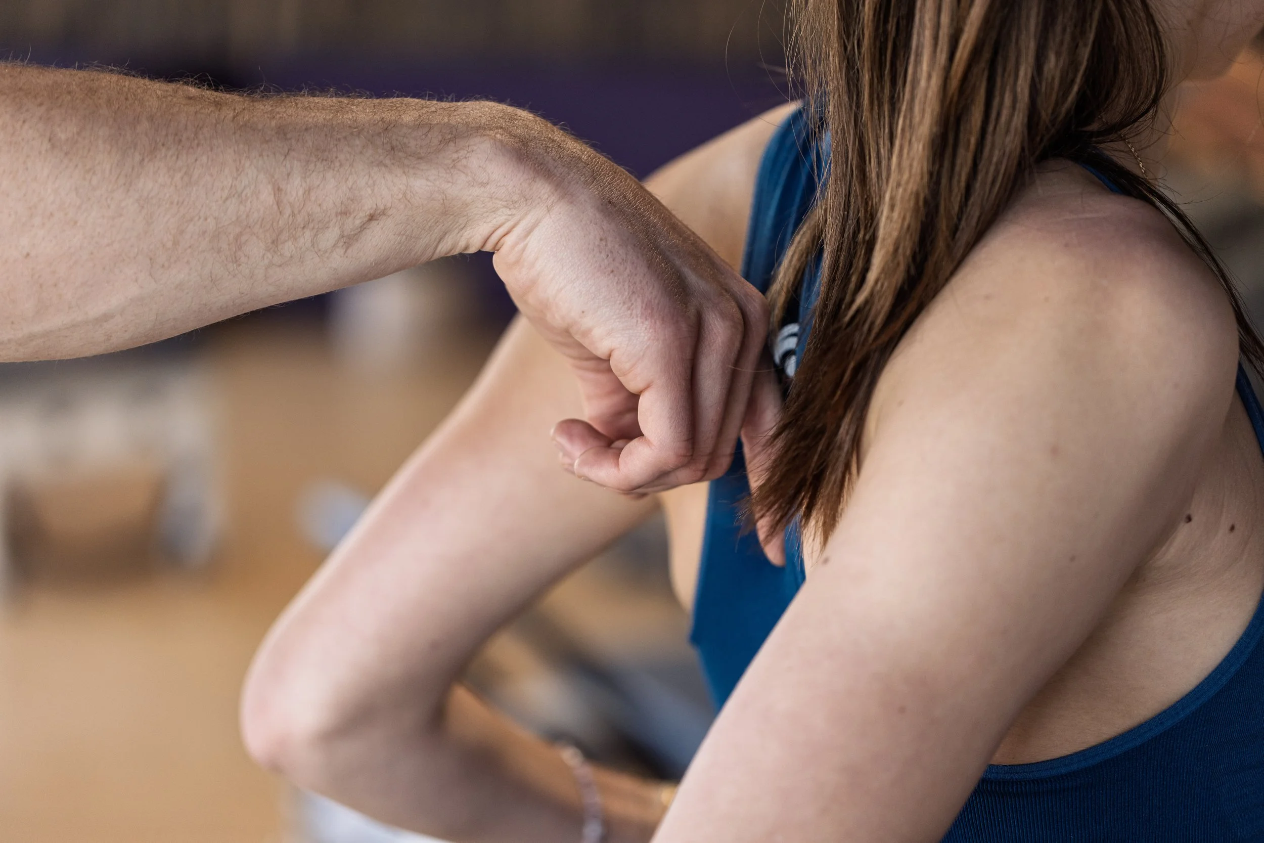 Un homme touche l'épaule d'une femme en portant un haut bleu, dans un cadre intérieur.