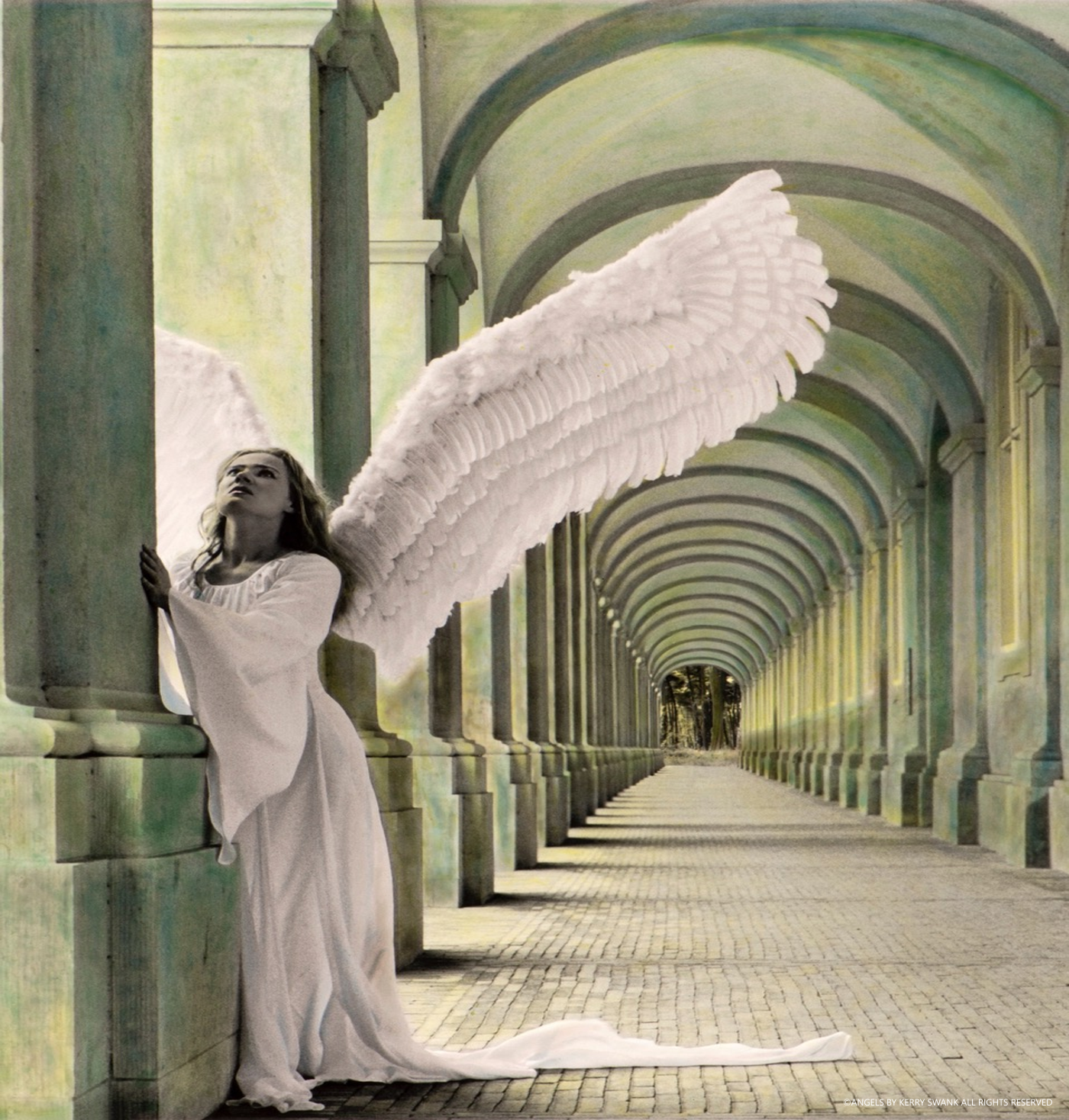 A woman dressed as an angel with large white wings, standing in a corridor with arches, looking upward with a contemplative expression.