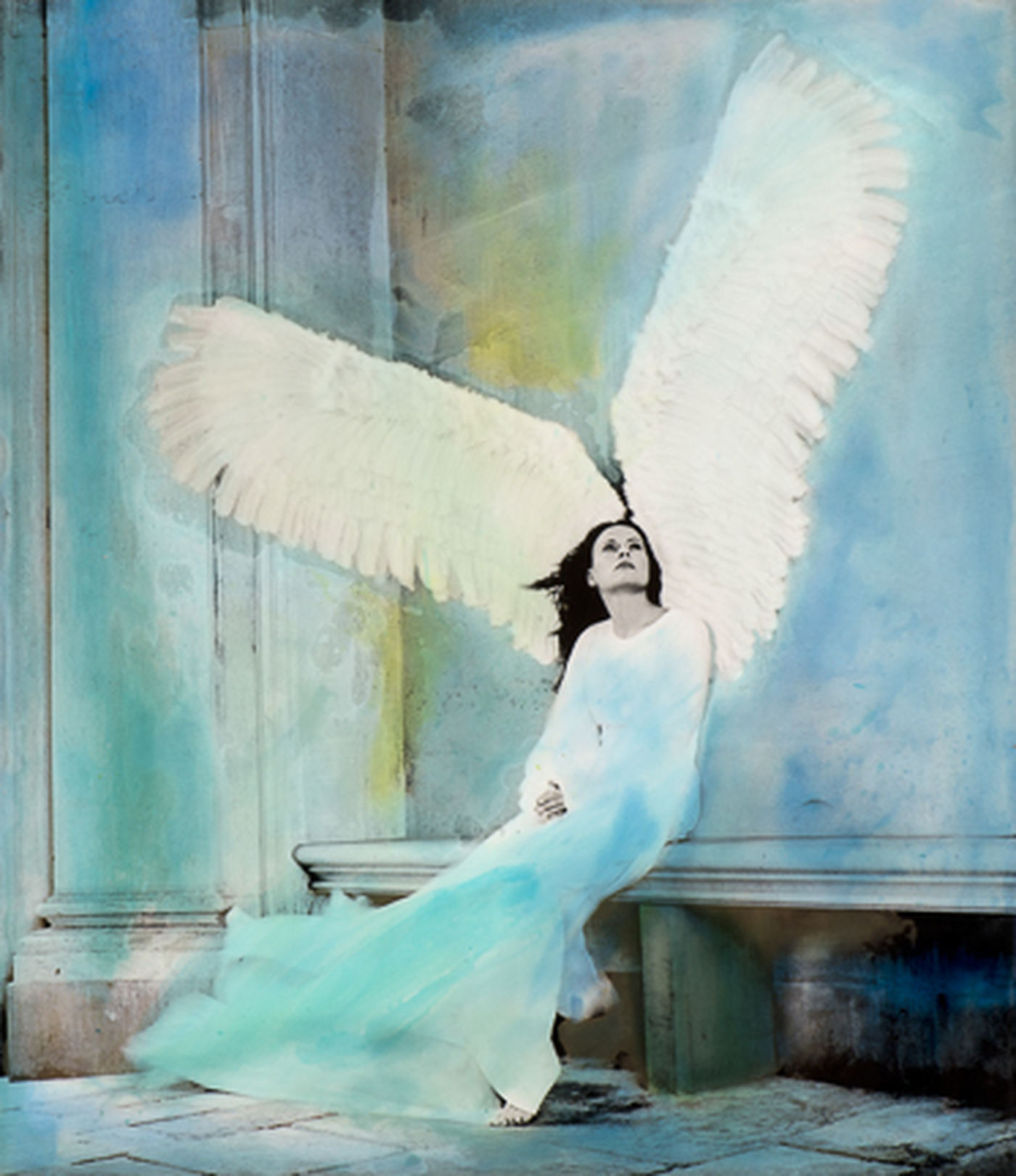 A mural of a woman with large white angel wings, sitting on a ledge with her eyes closed, in front of a blue and green painted background.