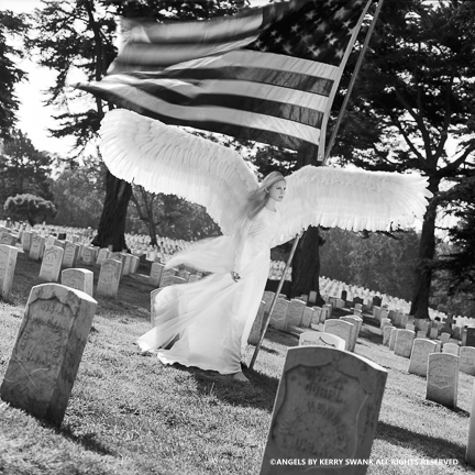A woman dressed as an angel with large wings holding an American flag in a cemetery.