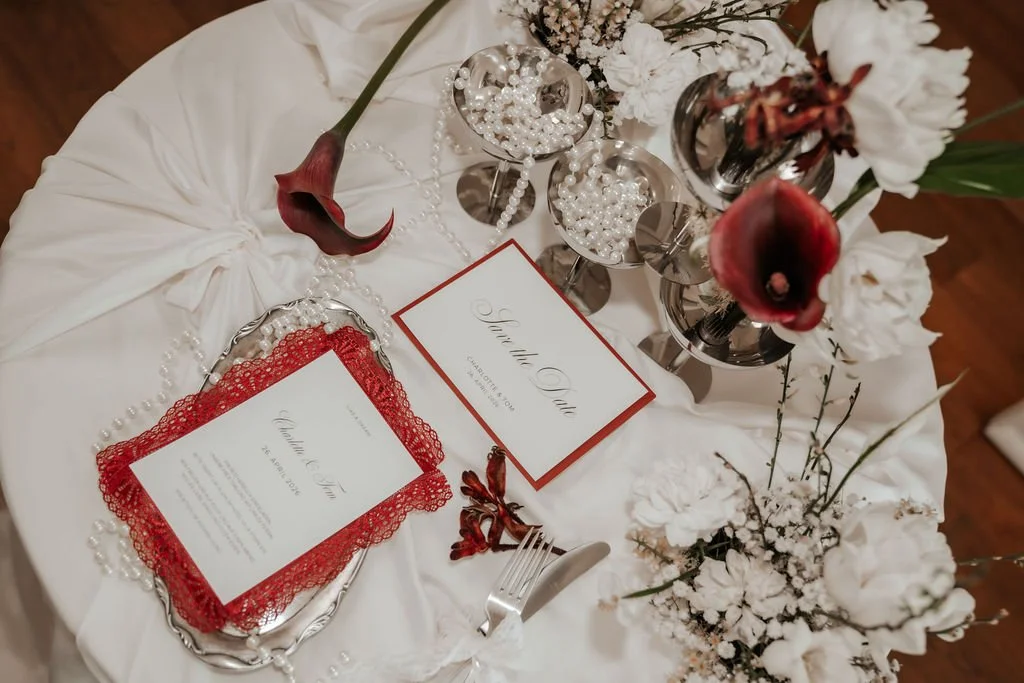 Ein festlich gedeckter Tisch mit weißen Blumen, Kerzen, Perlen und Einladungskarten, vermutlich für eine Hochzeit oder Feier.