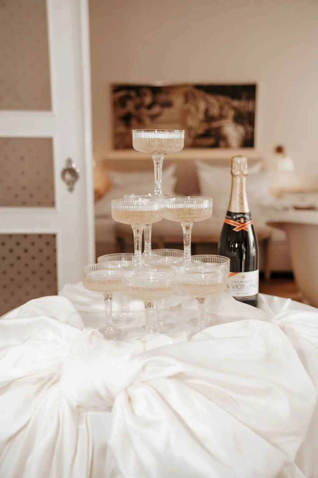 Sektgläser in einer Pyramide auf einem weißen Tuch, mit einer Flasche Sekt im Hintergrund.