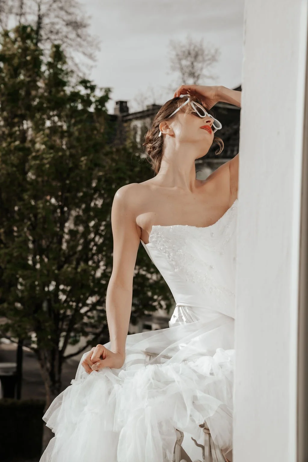 Frau in Hochzeitskleid, mit weißer Sonnenbrille, entspannt, draußen im Freien, with trees im Hintergrund.