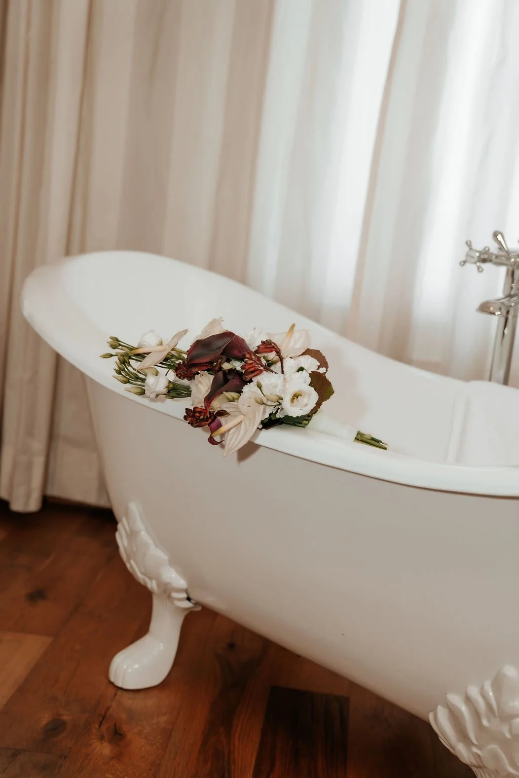 Weiße Badewanne mit Blumen auf der Kante, Holzfußboden, Vorhänge im Hintergrund