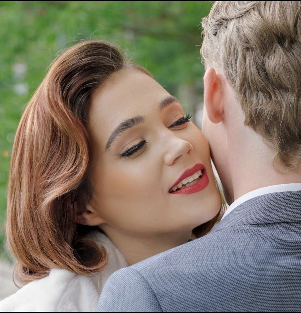 Ein Mann und eine Frau sind sehr nah beieinander, die Frau hat ihre Augen geschlossen und lächelt, während sie den Mann küsst.