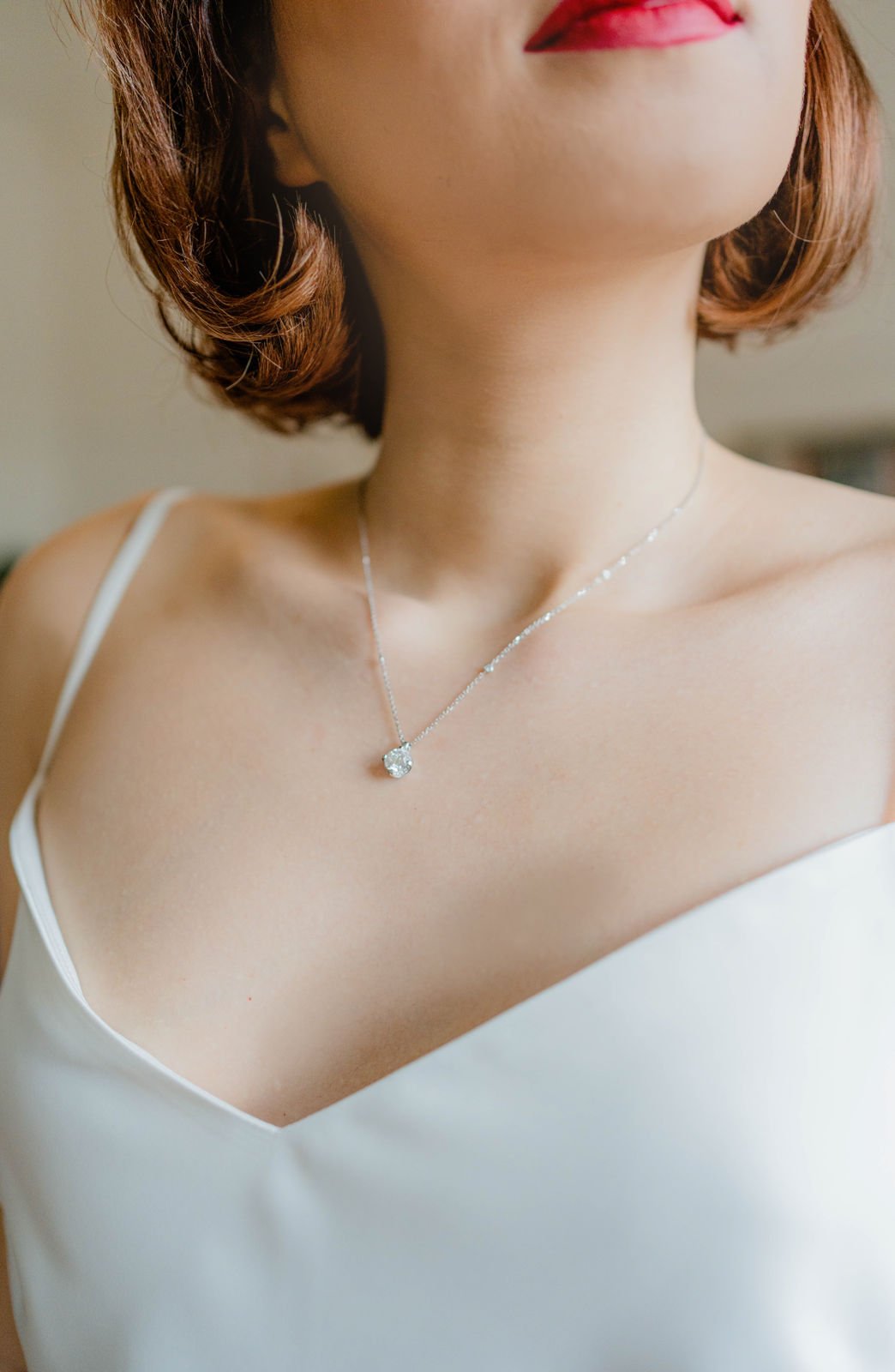Nahaufnahme eines Frauenhalses mit Silberkette und Anhänger, weiße Kleidung, welliges braunes Haar, rote Lippen.