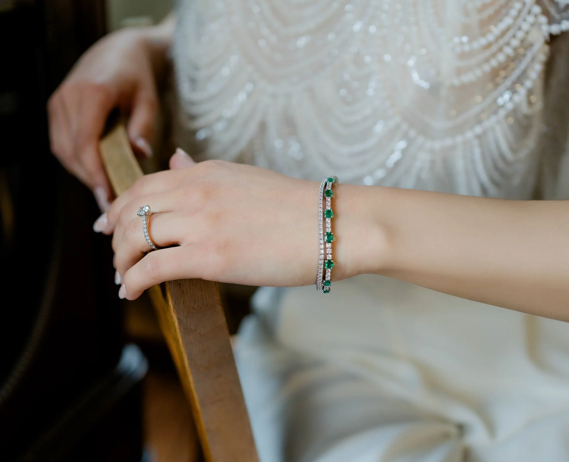Eine Hand trägt einen Verlobungsring und ein Armband mit grünen Edelsteinen, während die andere Hand eine Schmuckschatulle hält.