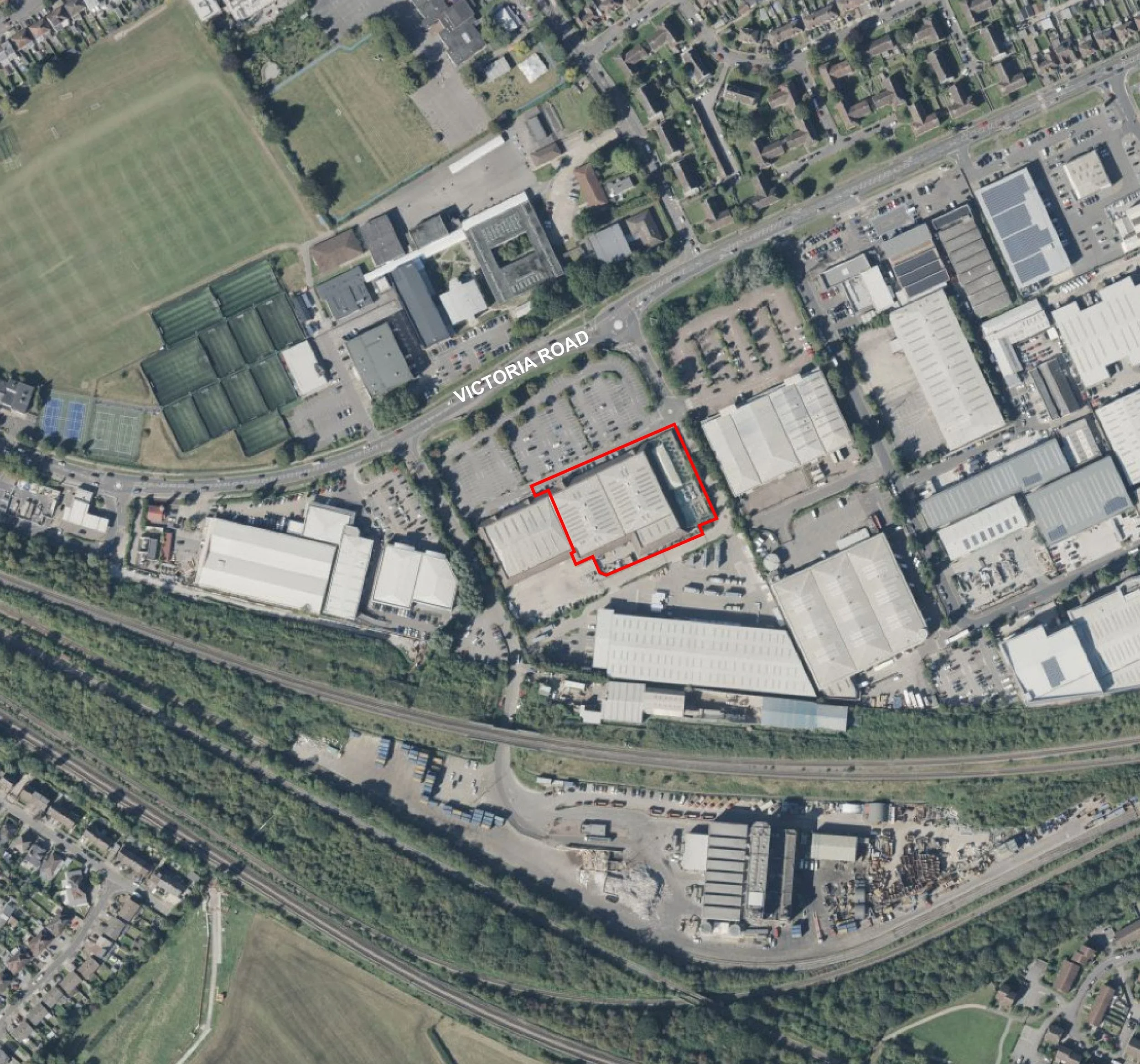 Aerial view of an industrial area with a marked building outlined in red, adjacent to Victoria Road, surrounded by parking lots, warehouses, green spaces, and a train track running along the bottom.