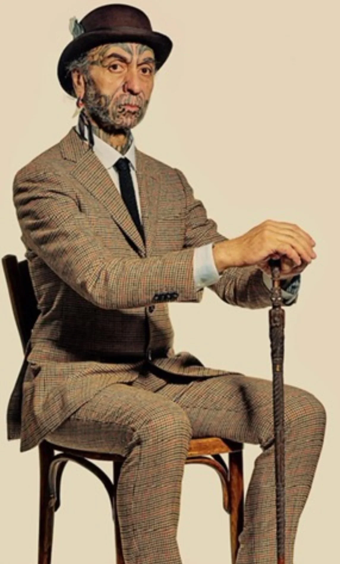 A man dressed in a vintage checkered suit, wearing a bowler hat, sitting on a chair, holding a cane, with a serious expression.