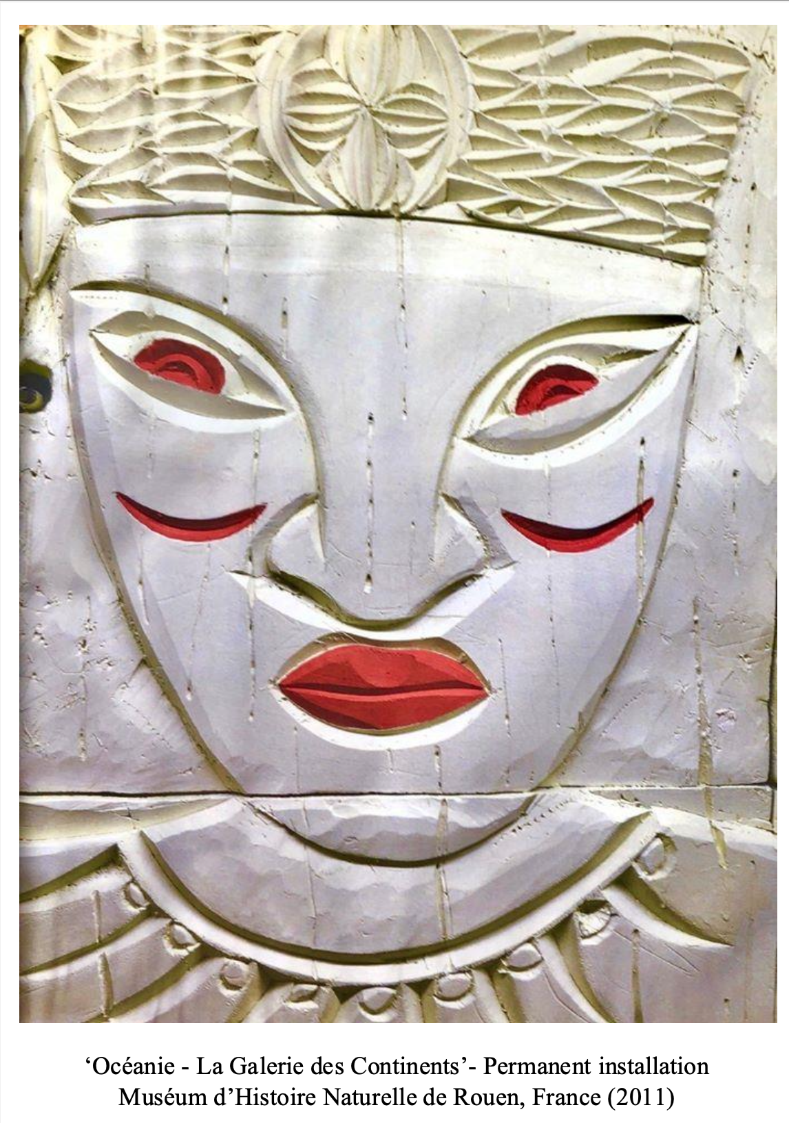 A close-up of a stylized face sculpture with a white face, red lips, and red accents around the eyes, part of a permanent installation at the Museum of Natural History in Rouen, France, created in 2011.