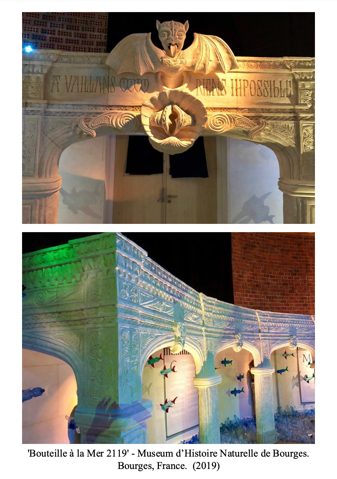 Sand sculpture of a medieval-style archway with a dragon or demon face at the top, featuring a bat-winged creature with an open mouth. The sculpture is detailed with intricate carved patterns and Latin inscriptions. Below, a colorful underwater-themed installation mimics a castle with columns and arches, illuminated with green and purple lights, and decorated with small fish sculptures.