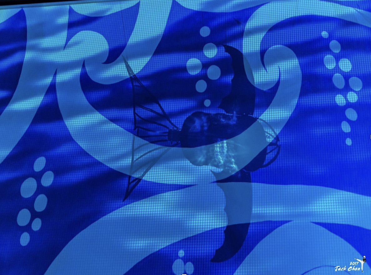 A blue underwater scene with a shark silhouette and bubbles, with abstract wave patterns and a signature in the bottom right corner.