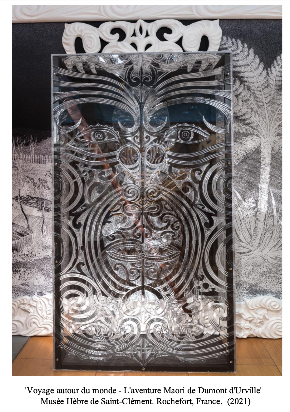 Intricate Maori-style carved wooden panel with symmetrical face design, displayed in a museum exhibit.
