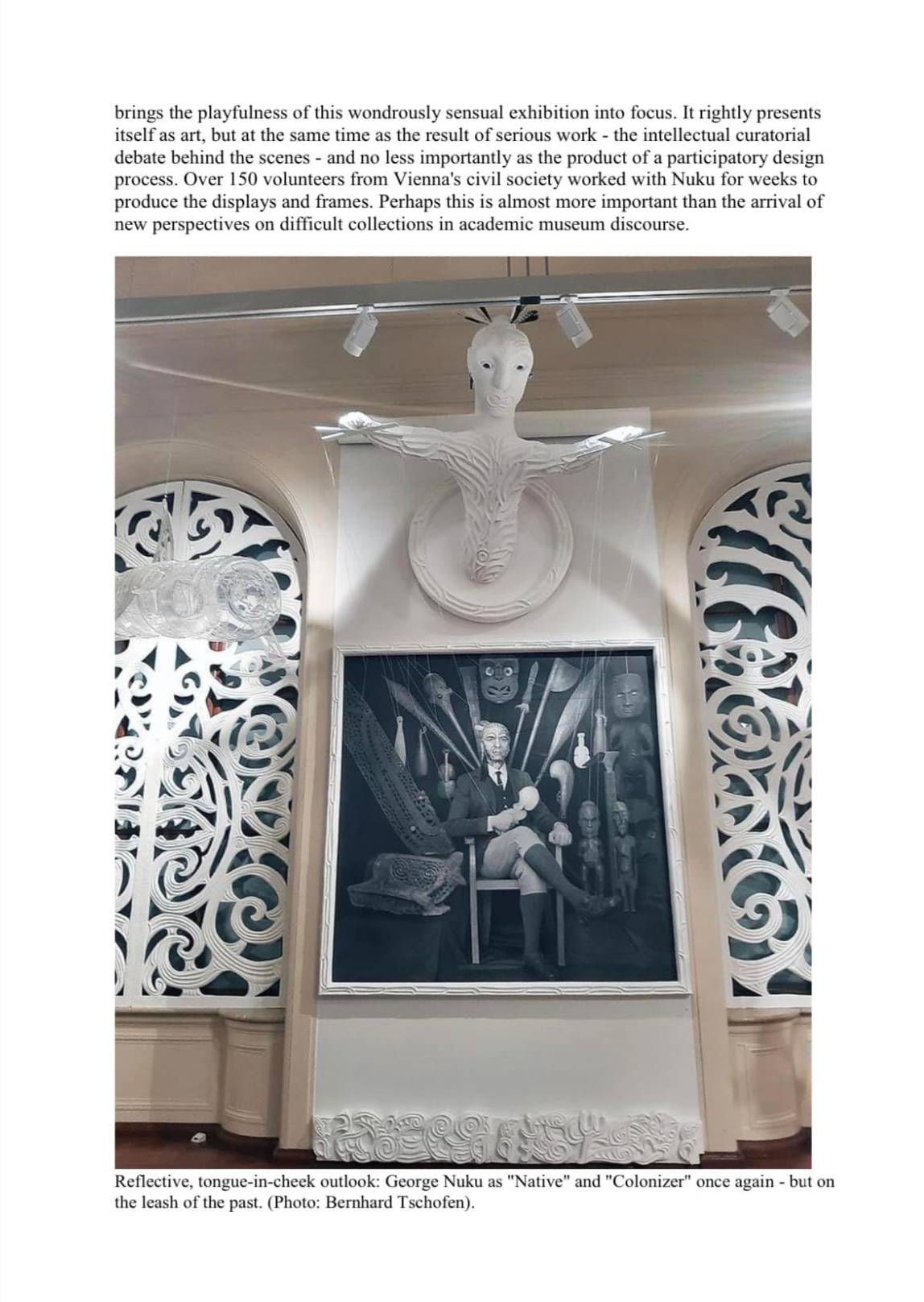 A display with a white sculpture of a face and outstretched arms mounted on the wall above a framed black and white portrait of George Nuku. The display features intricate, decorative patterns on side panels.