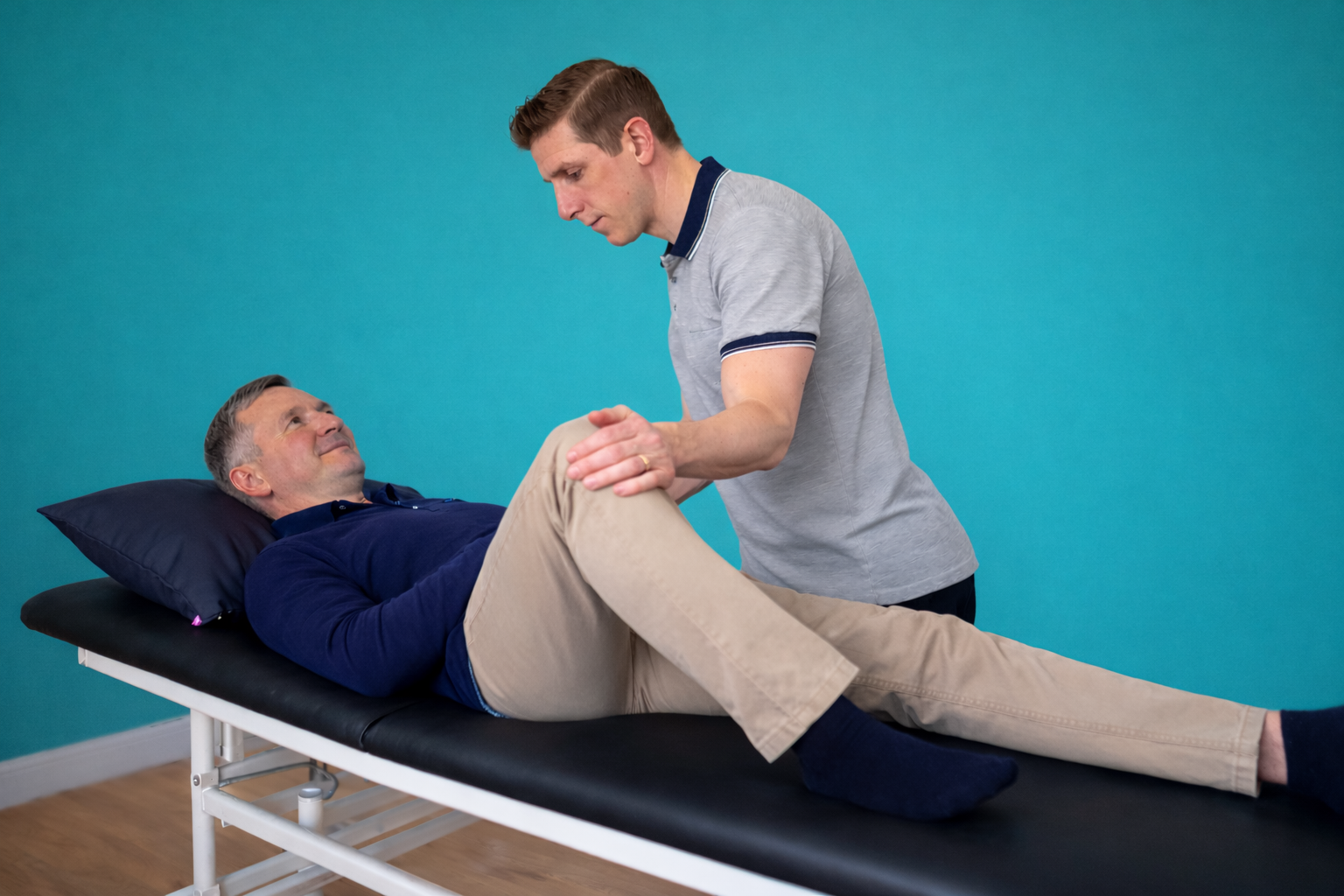 A physical therapist performs an assessment on a male patients leg on a treatment table.