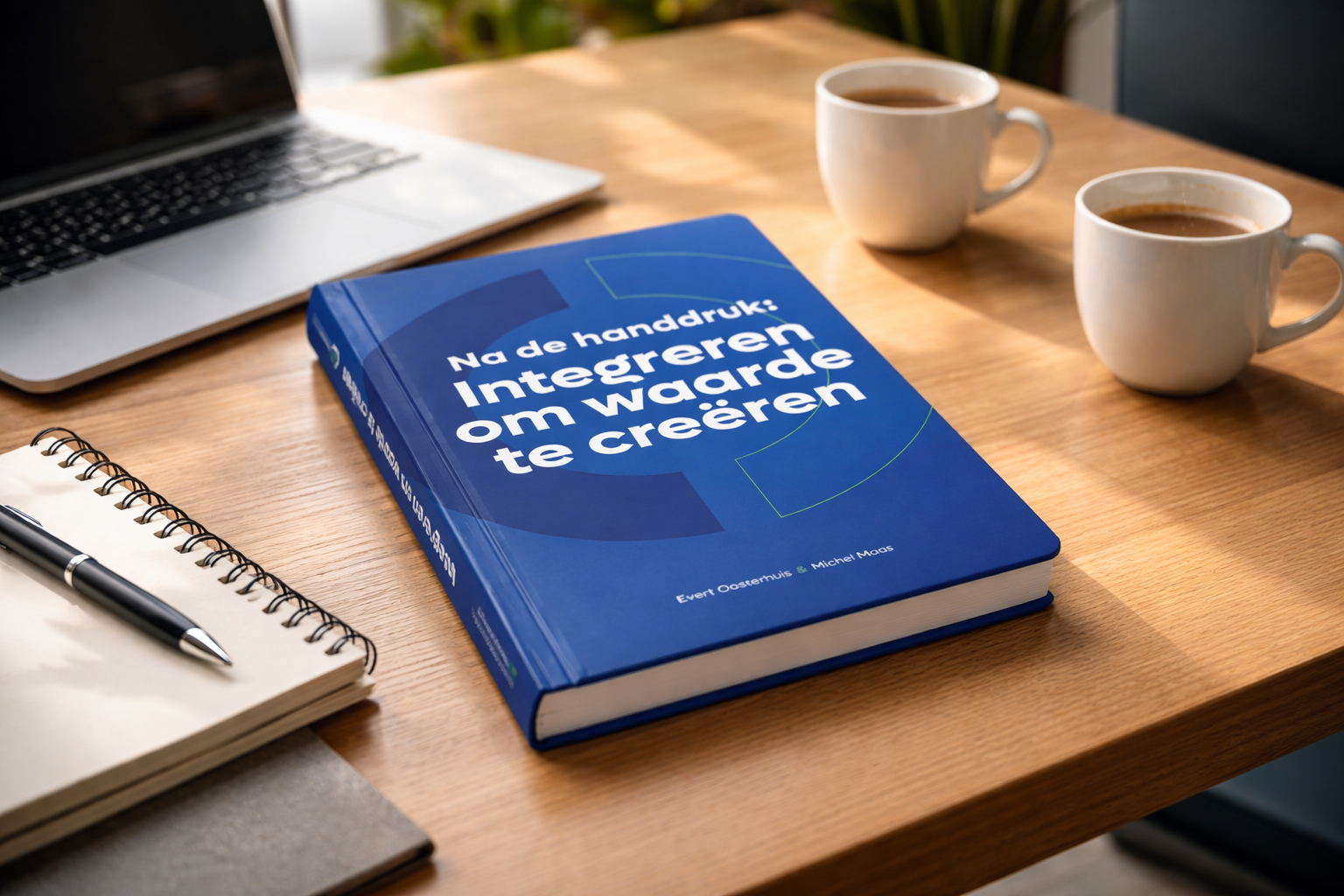 Een boek met de titel 'Na de handdruk: integreren om waarde te creëren', naast een open notitieboek, pen, laptop en twee kopjes koffie op een houten tafel.