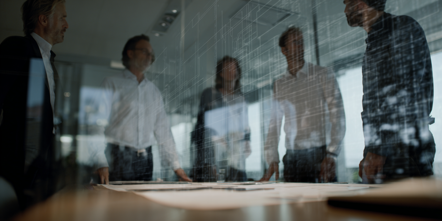 Vijf zakenmensen in een conferentiezaal bekijken een digitale projectie op een glazen muur.
