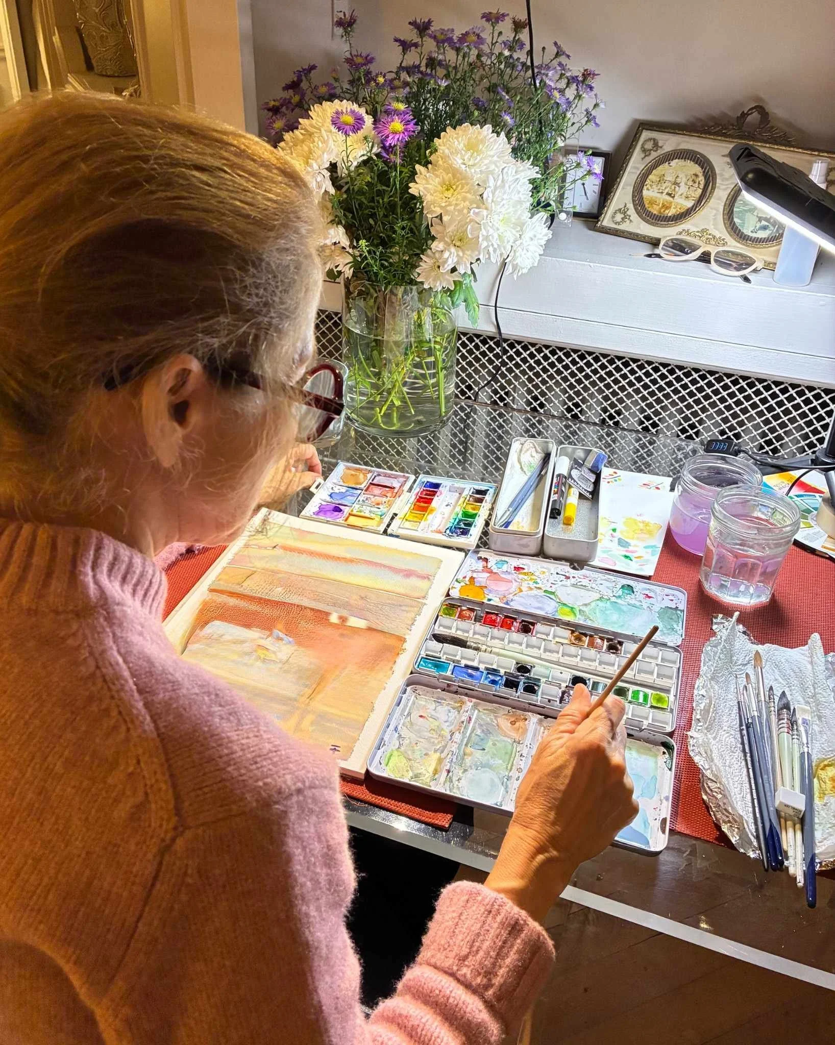 je peins assise à ma table avec mes palettes de couleurs et pinceaux, posé sur la table un bouquet de fleurs inspirants