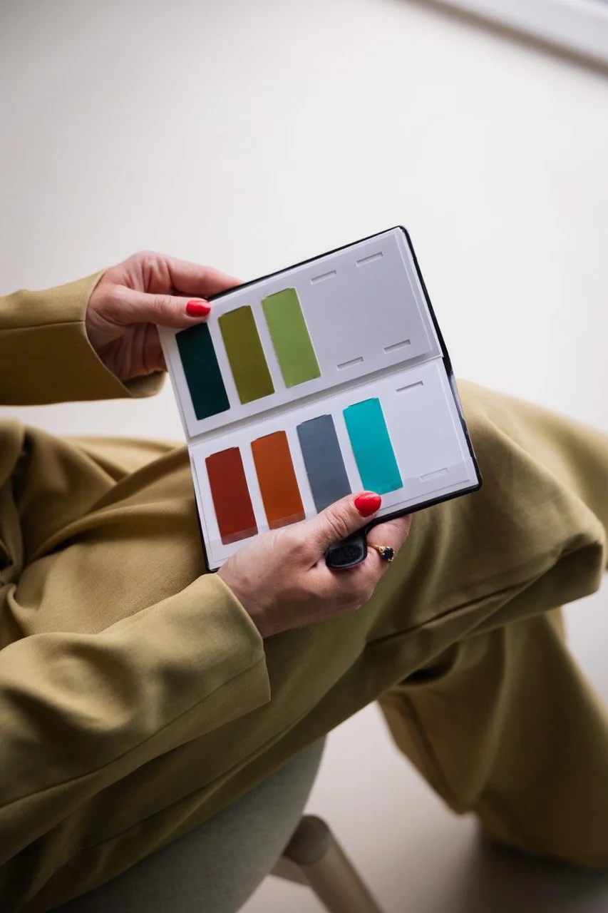 Elise houdt een kleurstaalkaart met verschillende kleuren in de hand, zittend met gekleurde kleding.