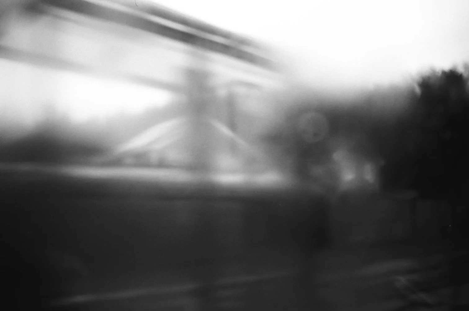Blurred black-and-white photo of a house in the distance, with trees and a street in the foreground.