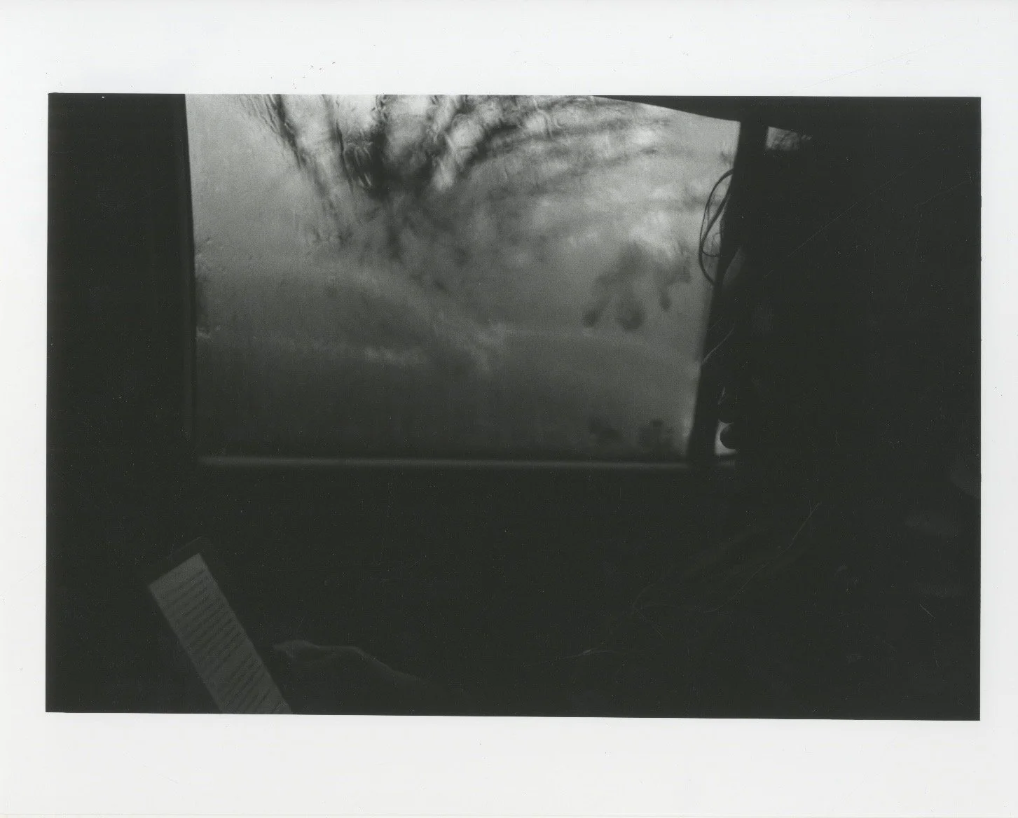 Black and white indoor scene with a window showing an outdoor view of bare trees and the sky.