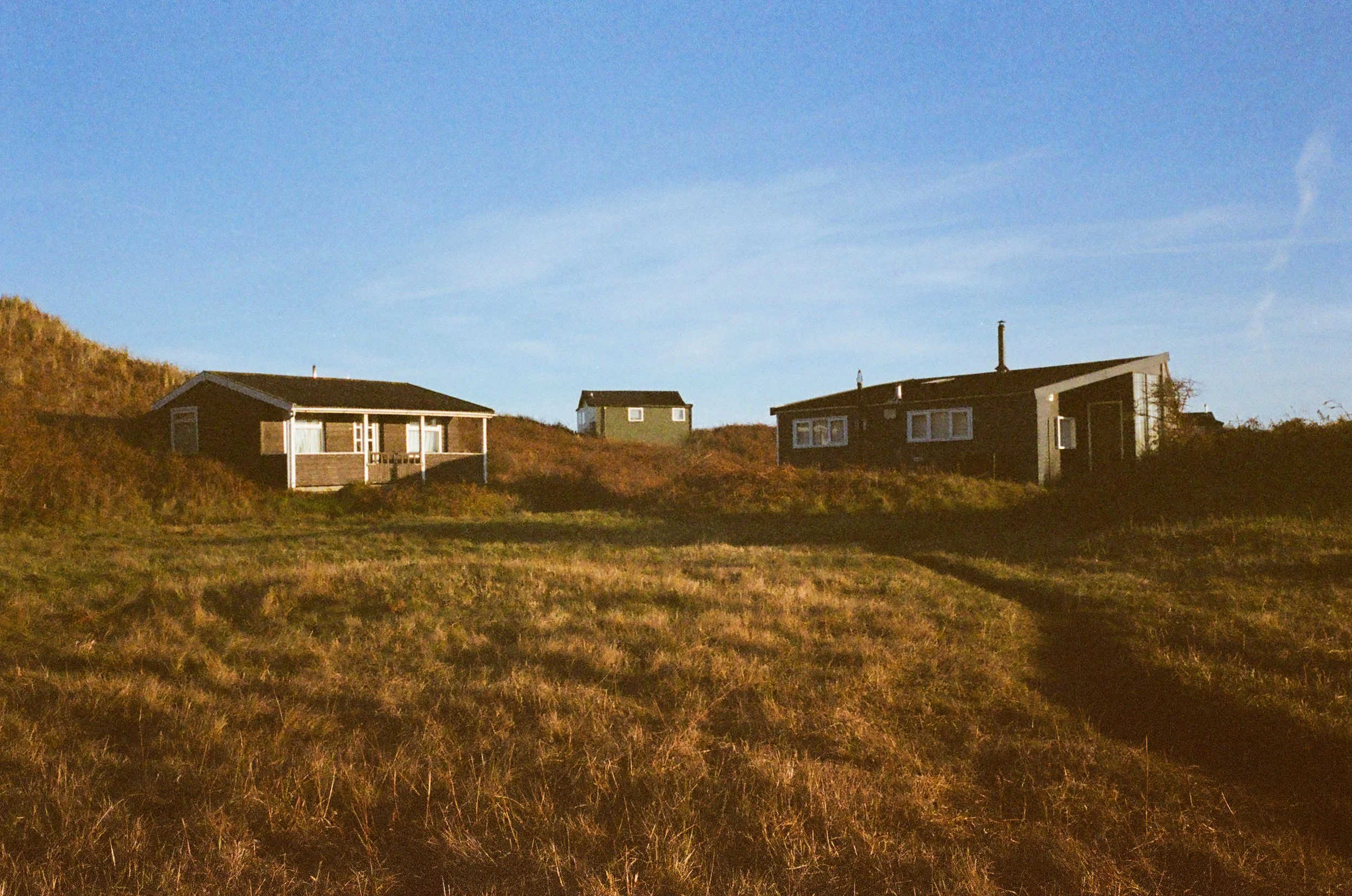 Three houses on a grassy hillside under a clear blue sky.