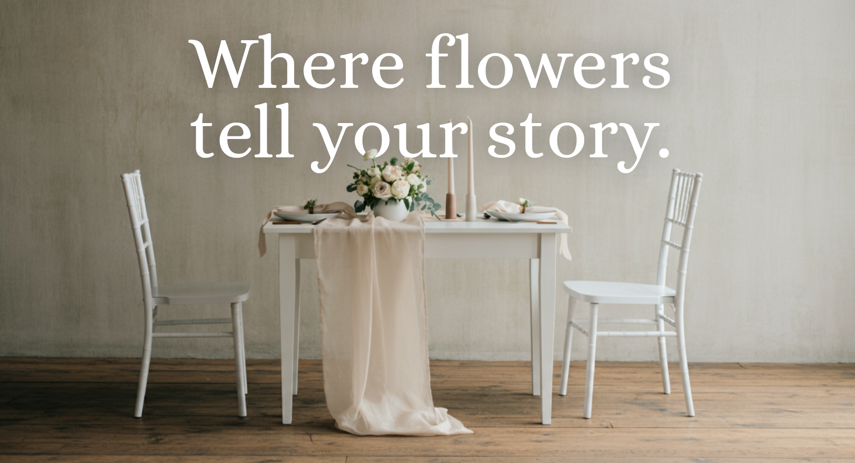 A white dining table with a beige tablecloth, floral centerpiece, and candles, set against a plain wall with the text 'Where flowers tell your story.'