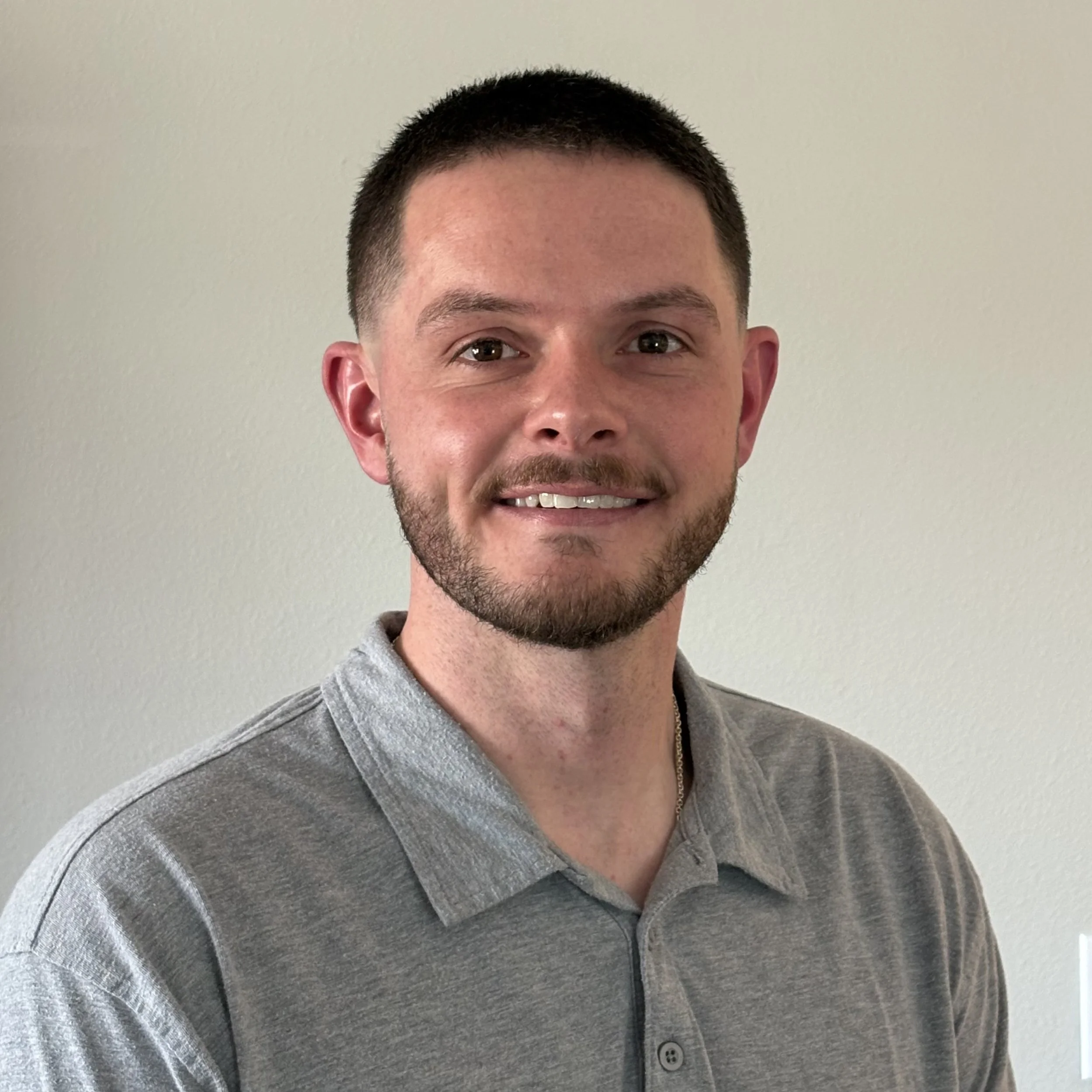 Austin Perry: A young man with short dark hair, a trimmed beard, and wearing a gray polo shirt, smiling at the camera.