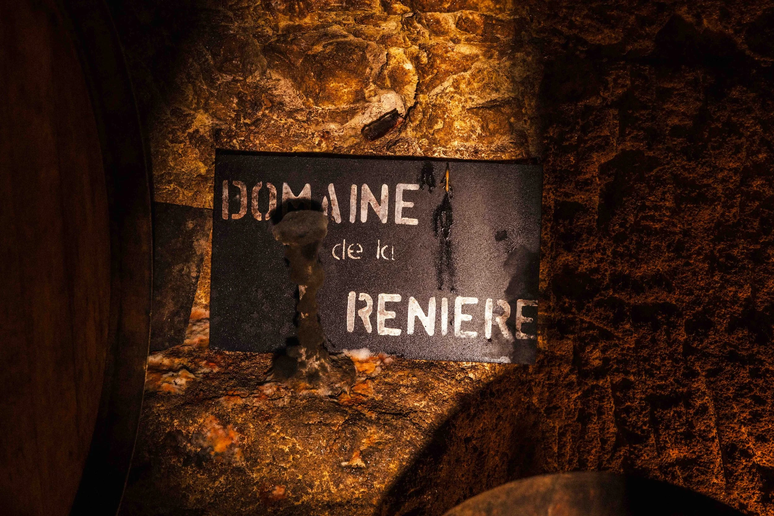 Plaque en métal noir avec inscription partiellement visible: "DOMAINE de la RENAISSANCE", fixée à une surface rocheuse.