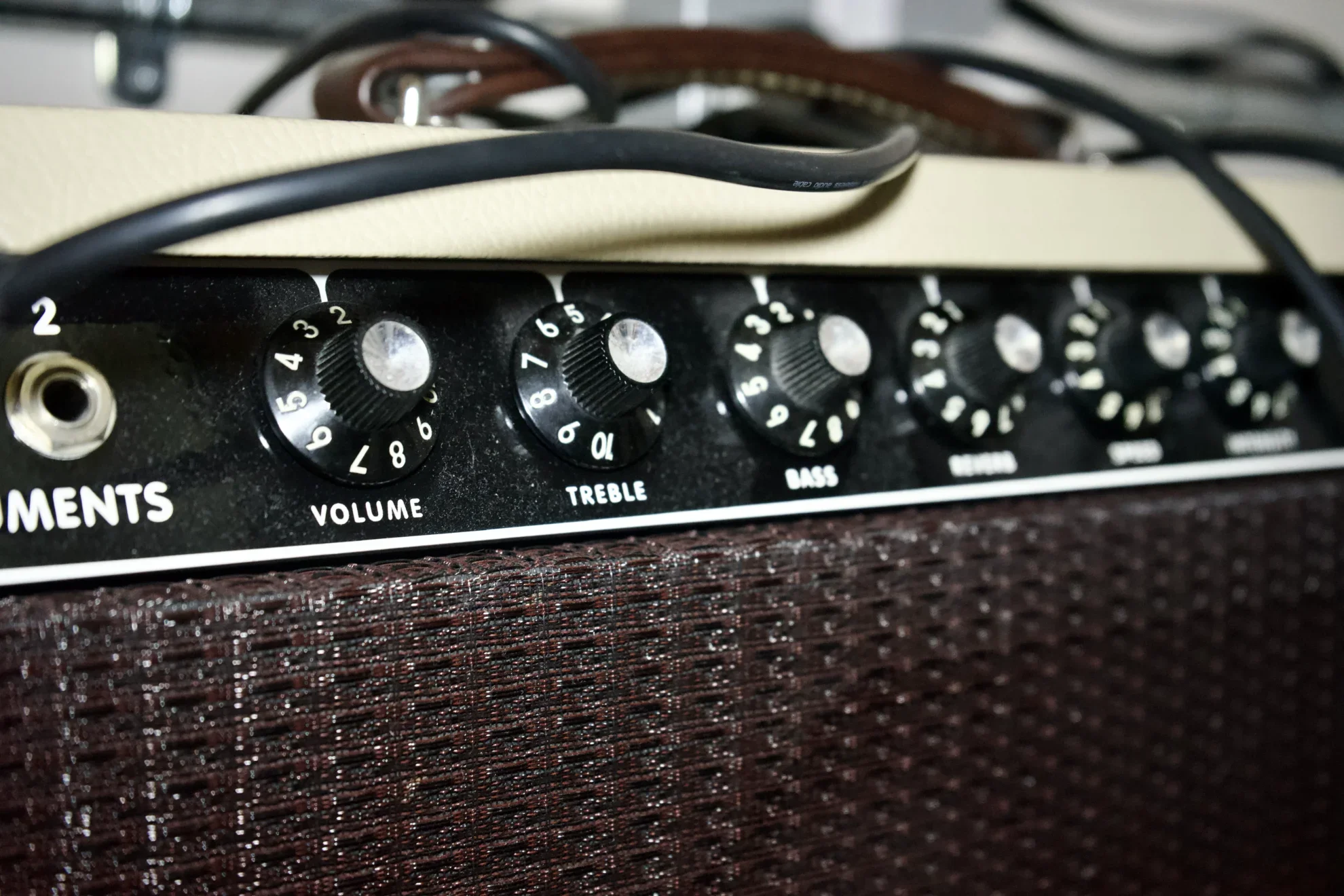 Close-up of a guitar amplifier control panel with knobs for volume, treble, bass, mids, and other settings, with cables connected on top.