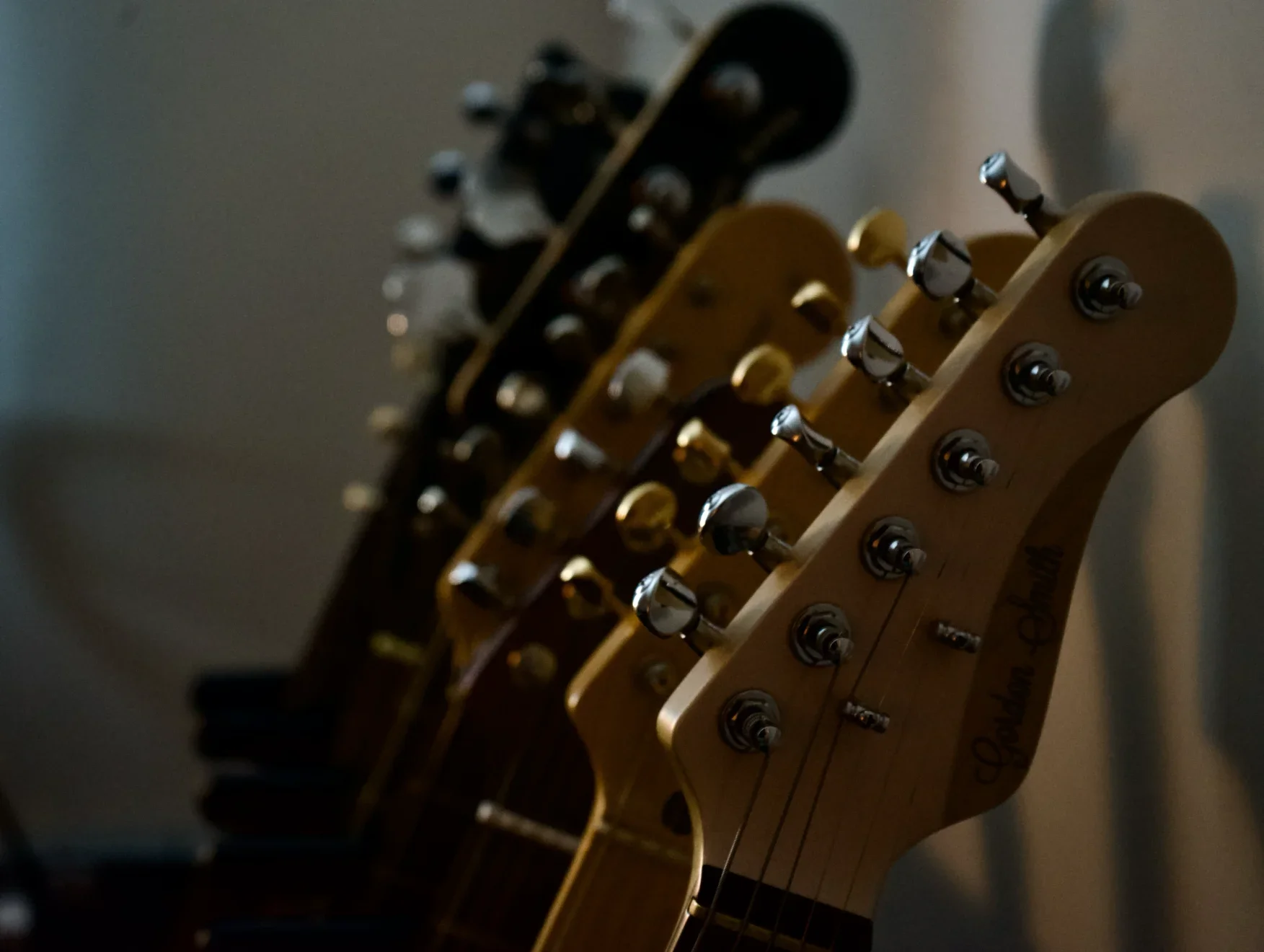 Multiple electric guitars with headstocks and tuning pegs in a row, shot in dim lighting.