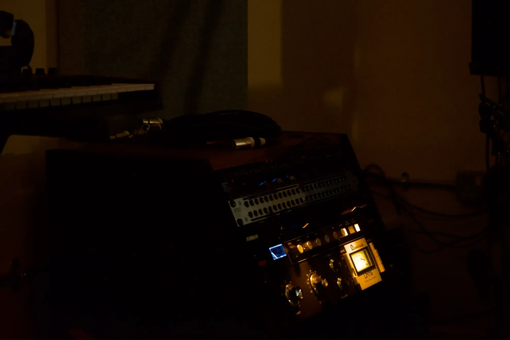 A dimly lit music studio with a keyboard on a stand, a MIDI controller, a mixer, and a DJ or sound equipment with illuminated dials and a display.
