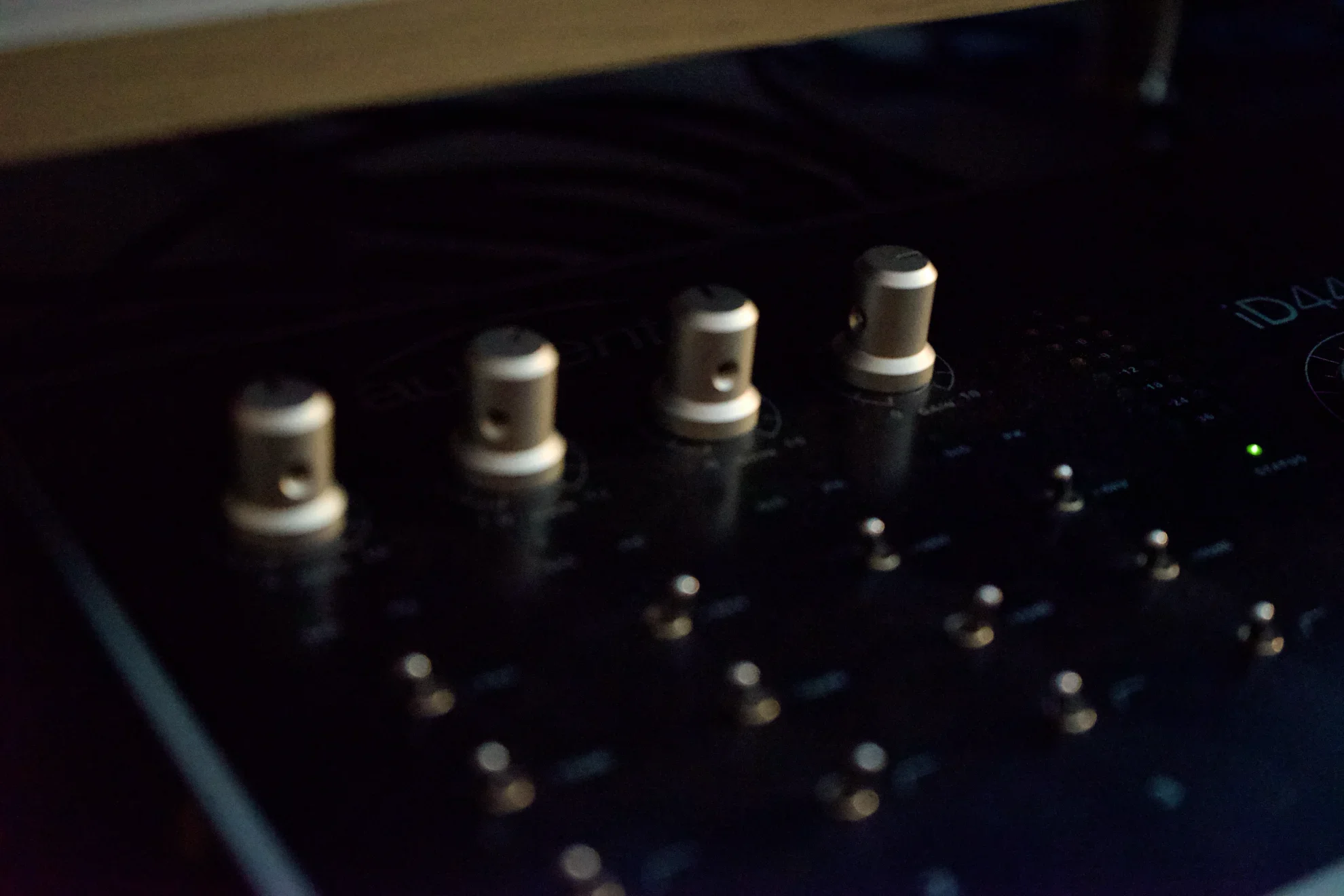 Close-up of a music mixer with four silver knobs, buttons, and a small green LED light on a dark background.