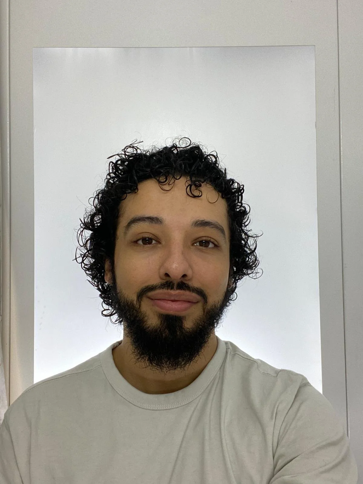A man with curly black hair and a beard taking a selfie in front of a mirror.