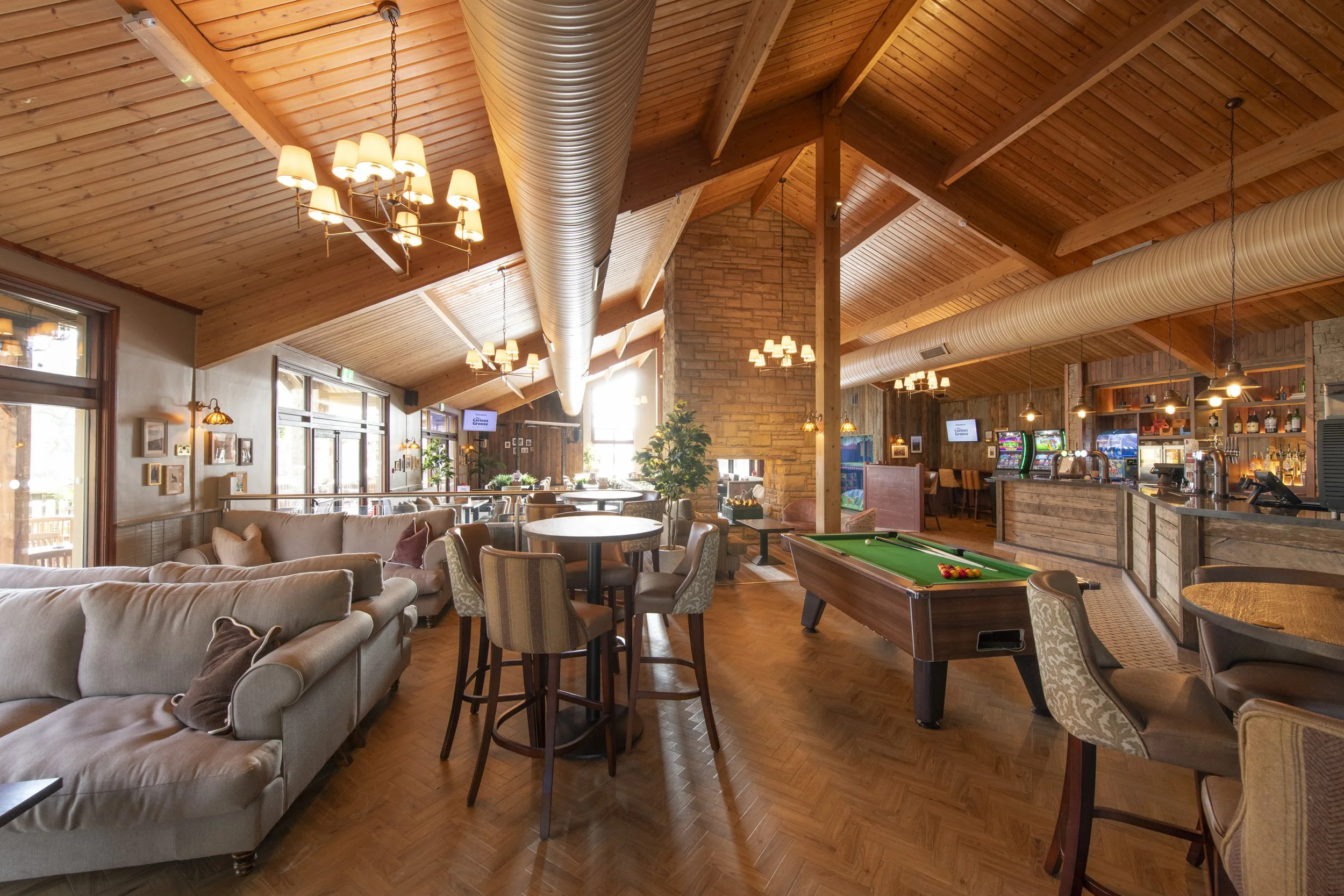Pool table amongst tables, chairs and sofas; there's a stone central fireplace and a bar in the background.