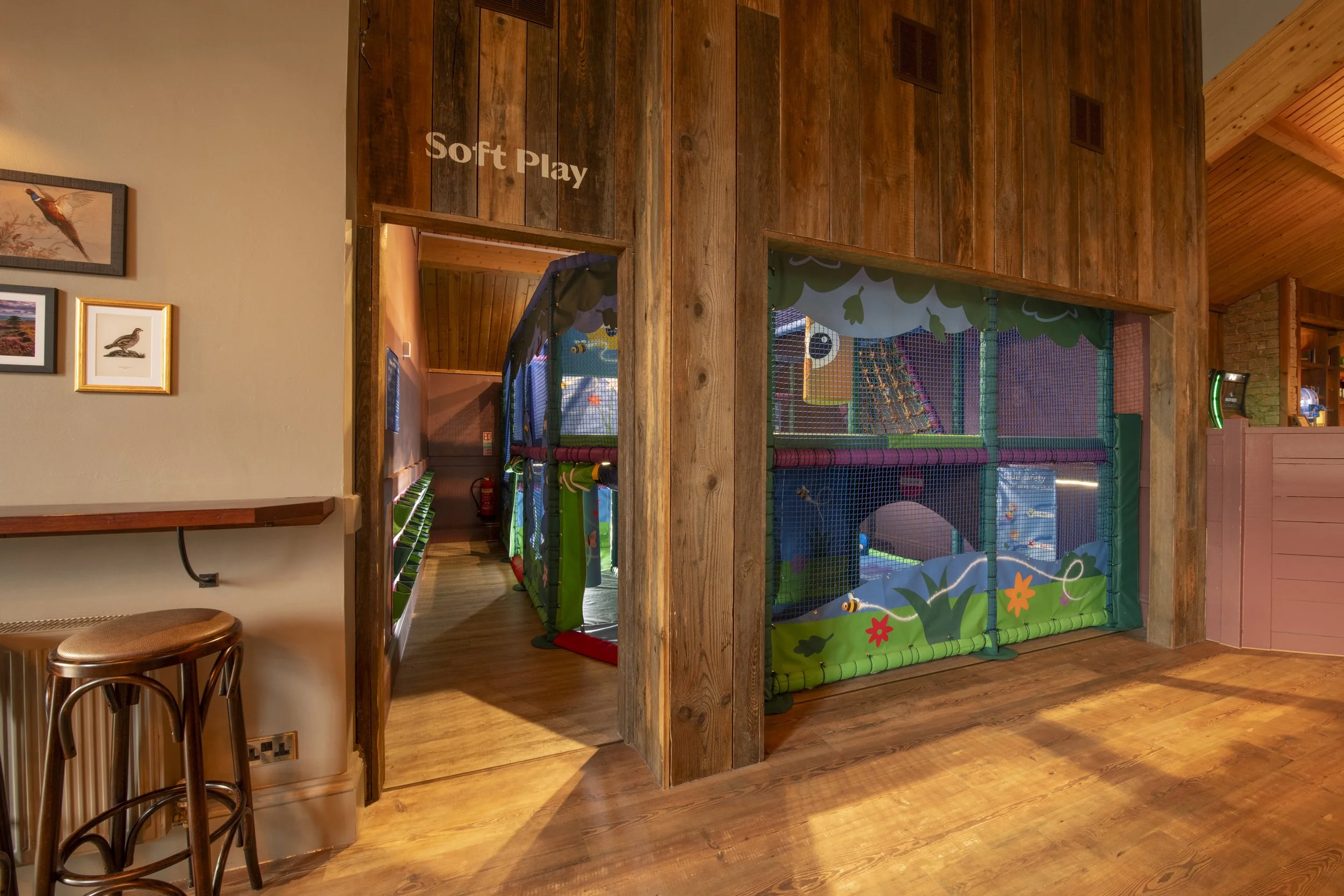 Two young boys playing on indoor jungle gym with slides and padded surfaces, smiling and having fun.