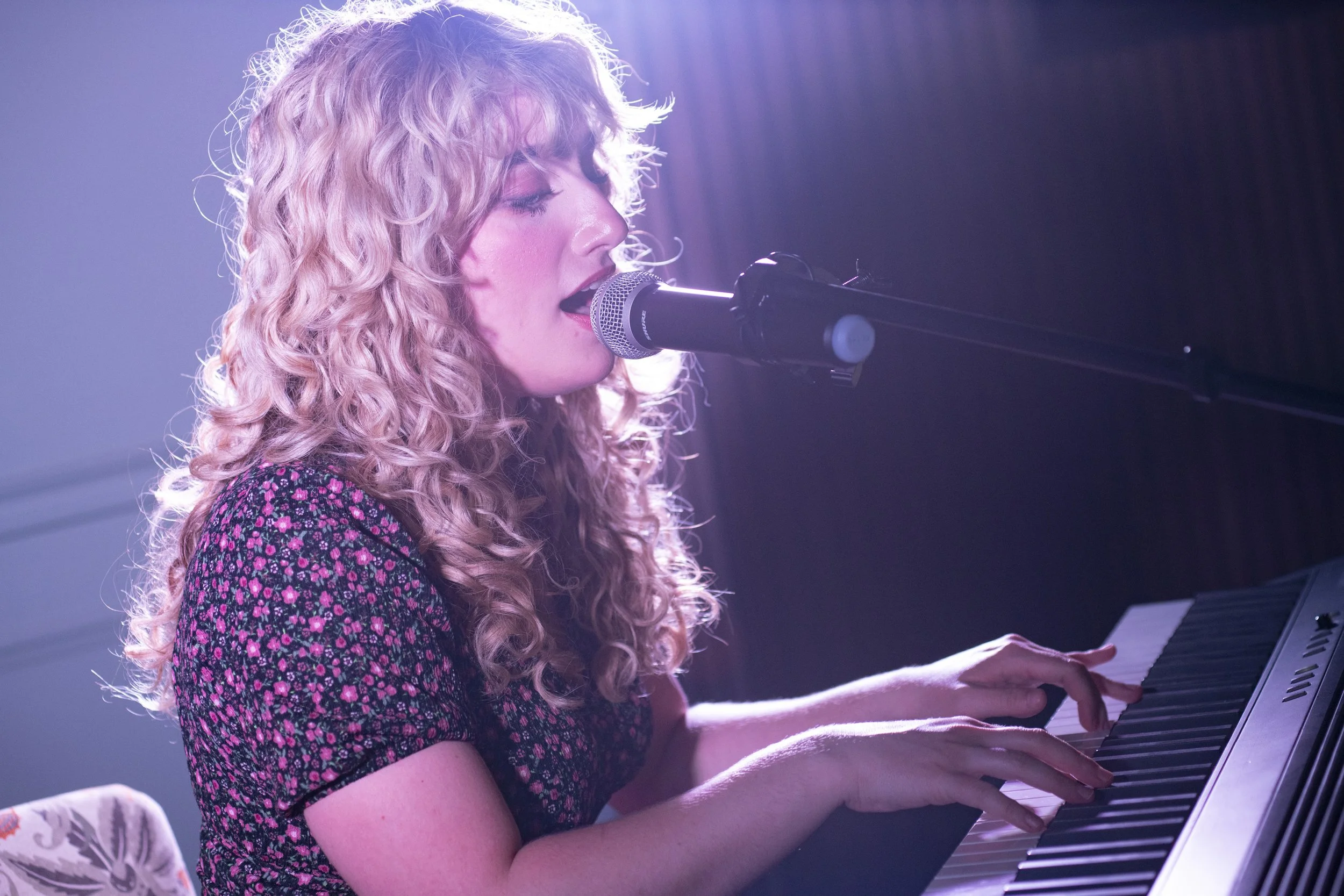 A female musician is performing on a stage, playing keyboard and singing at the same time.