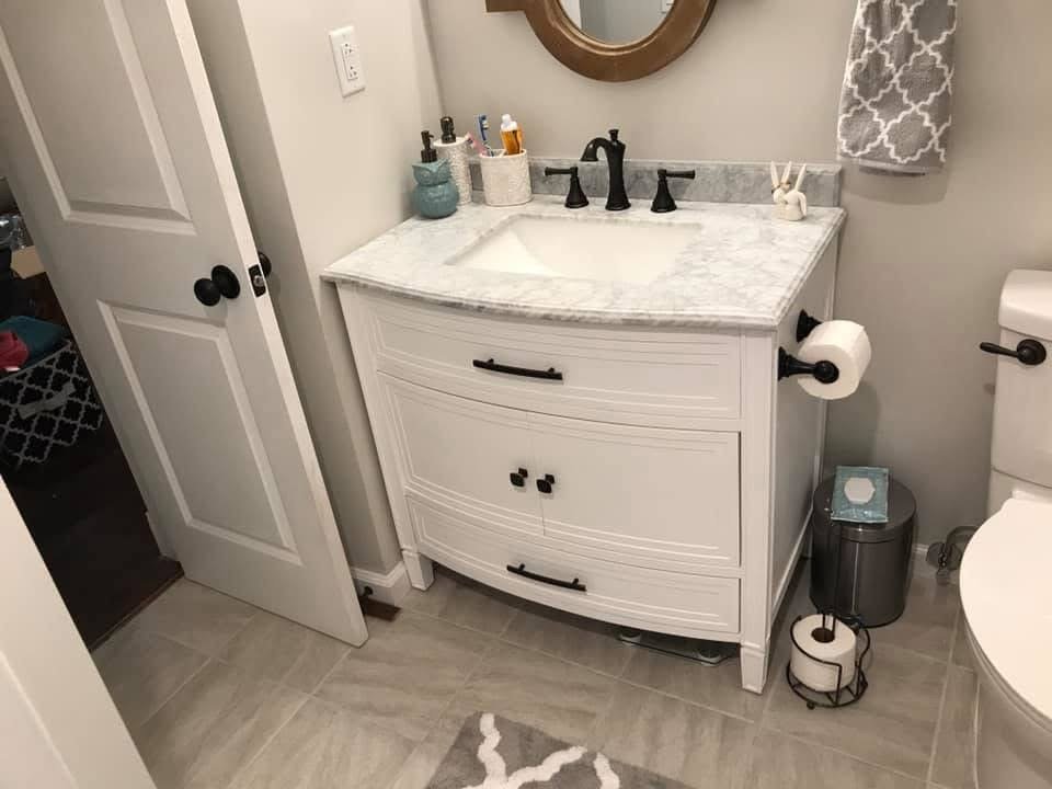 Bathroom vanity with a marble countertop, black faucet, and white cabinet drawers, with a mirror above, a towel, and a toilet nearby.