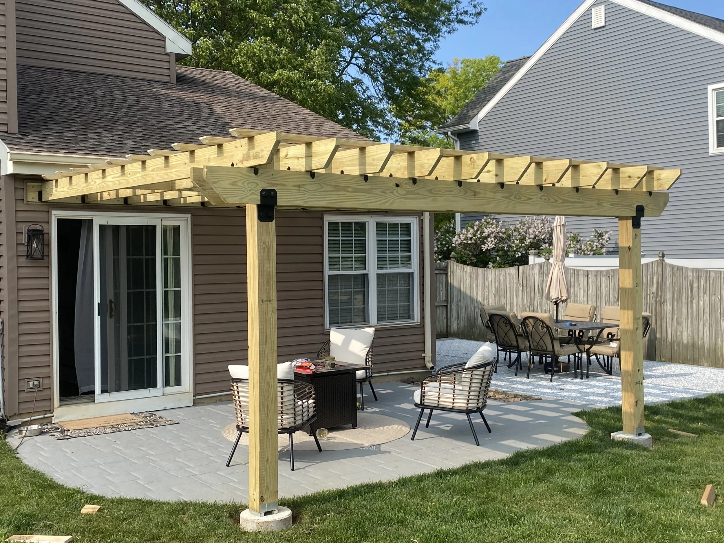 In-progress wooden pergola construction on backyard patio, with outdoor furniture and neighboring houses