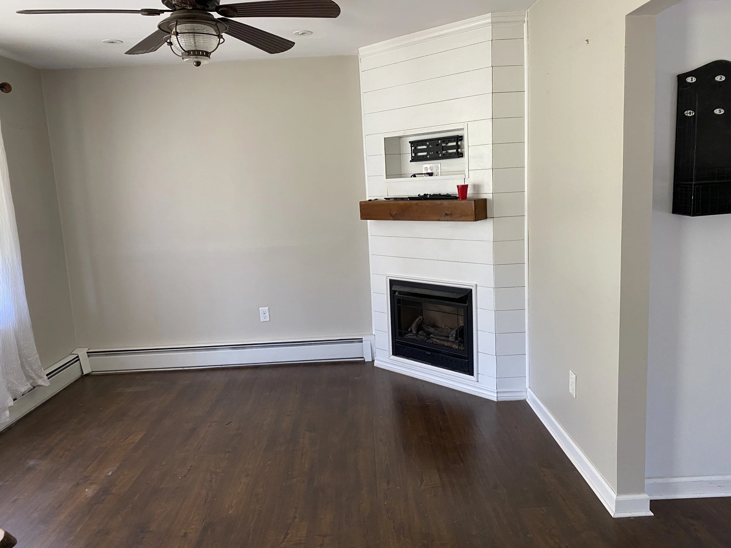 Empty living room with hardwood floors, a fireplace, a ceiling fan, and a wall-mounted TV bracket.