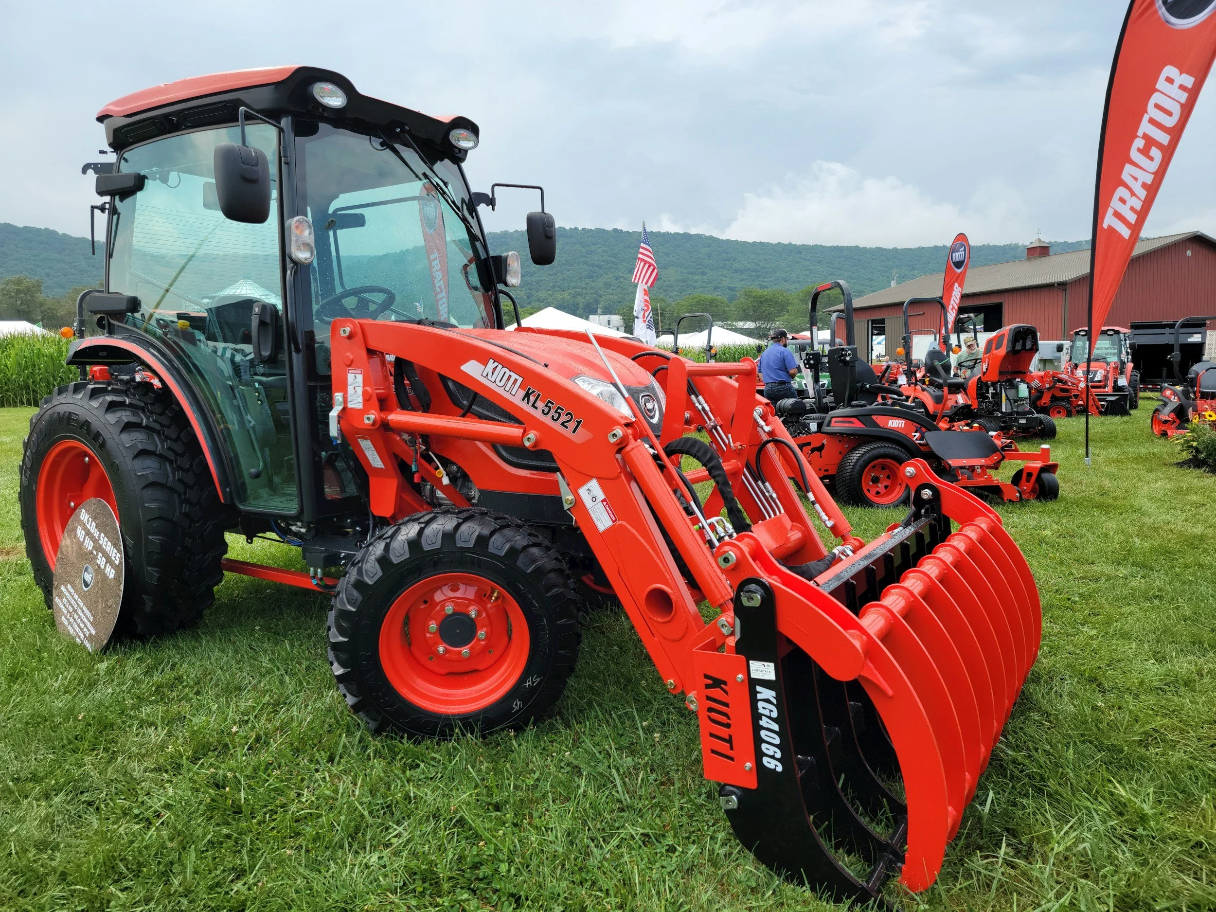Several red tractors with black tires displayed outdoors at an agricultural equipment show, with a red barn and green mountains in the background.