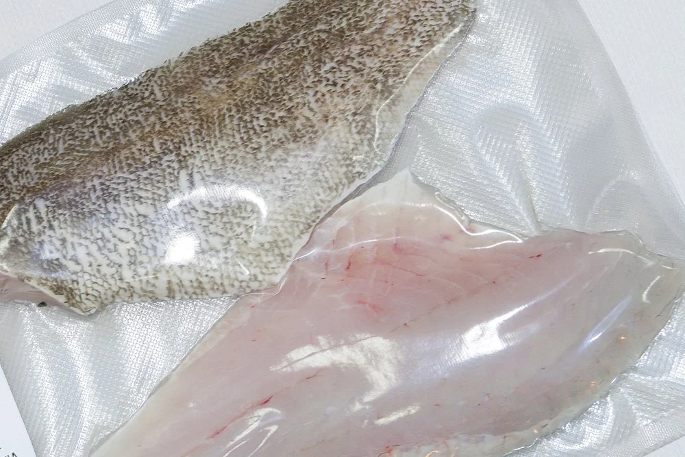 Two vacuum-sealed fish fillets, one with skin and one without, placed on a textured surface.