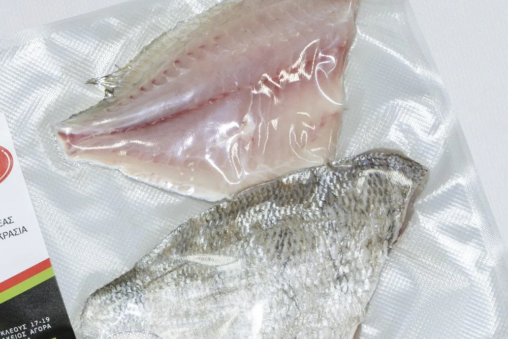 Two pieces of raw fish, one fillet with silver scales and one skinless fillet, on plastic packaging.